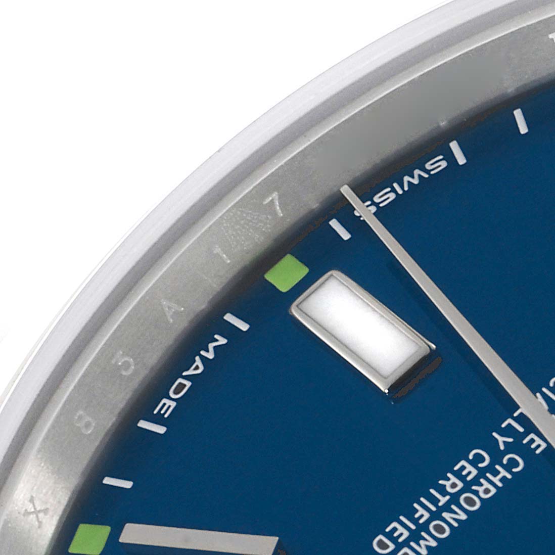 The image shows a close-up of the dial and markers of a Rolex Oyster Perpetual 114300 Men's Stainless Steel Blue Dial 114300 Men's Stainless Steel Blue Dial, viewed from an oblique angle.