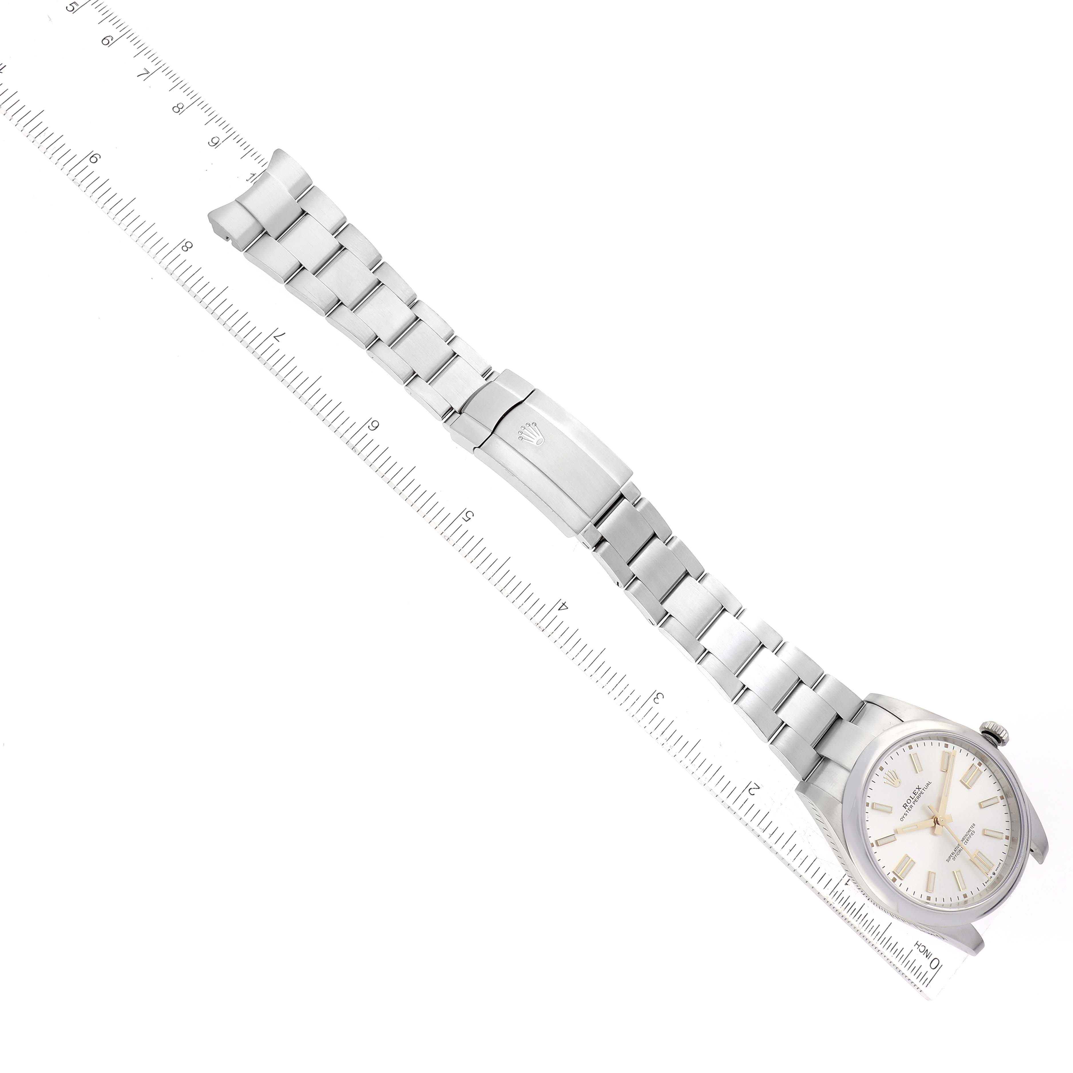 The image shows a Rolex Oyster Perpetual 124300 Men's Stainless Steel Silver Dial 124300 Men's Stainless Steel Silver Dial watch from an overhead angle, displaying the face, bracelet, and clasp next to a ruler.