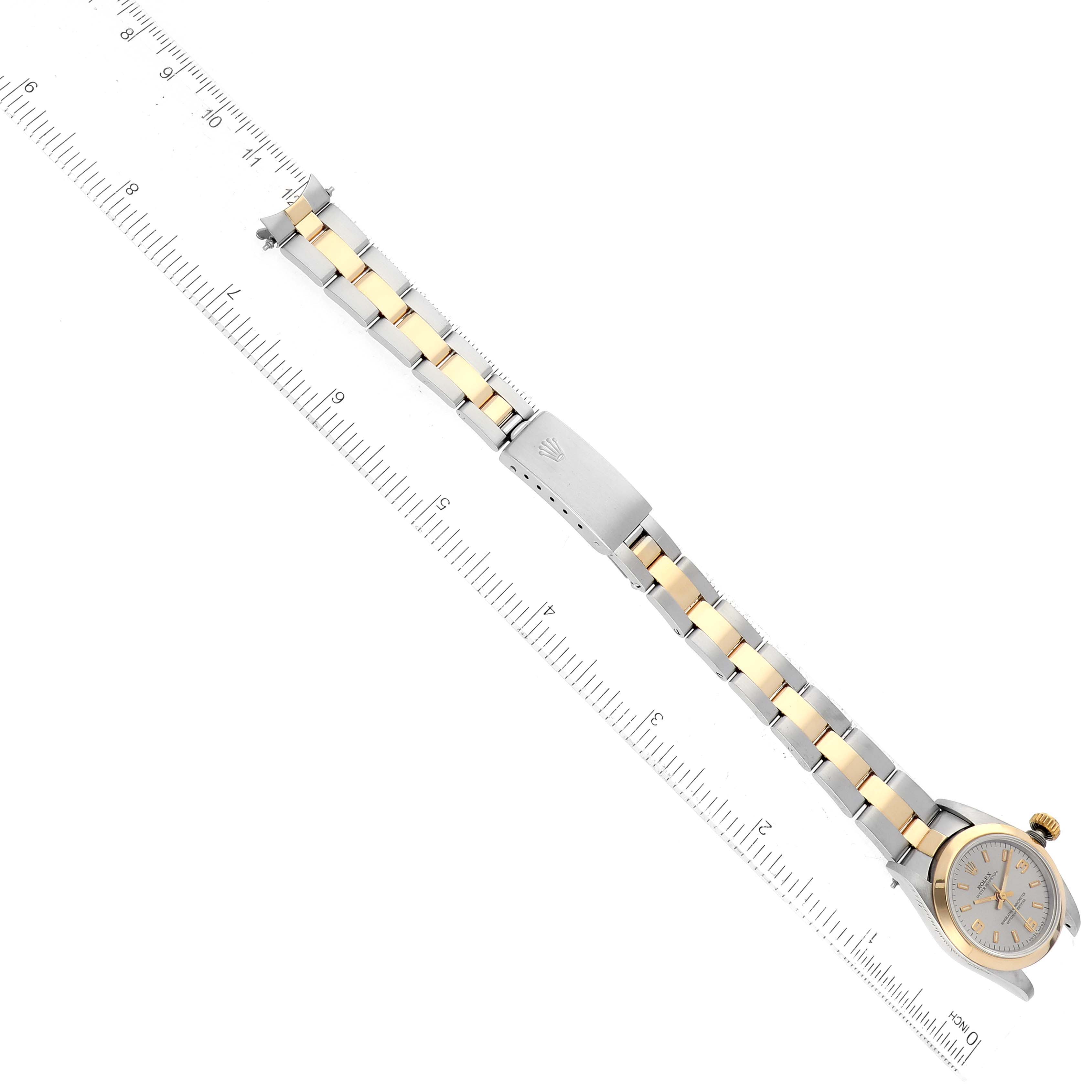The image shows a top view of a Rolex Oyster Perpetual 67183 Women's Steel and Gold (two tone) Silver Dial 67183 Women's Steel and Gold (two tone) Silver Dial watch with its bracelet fully extended alongside a ruler.