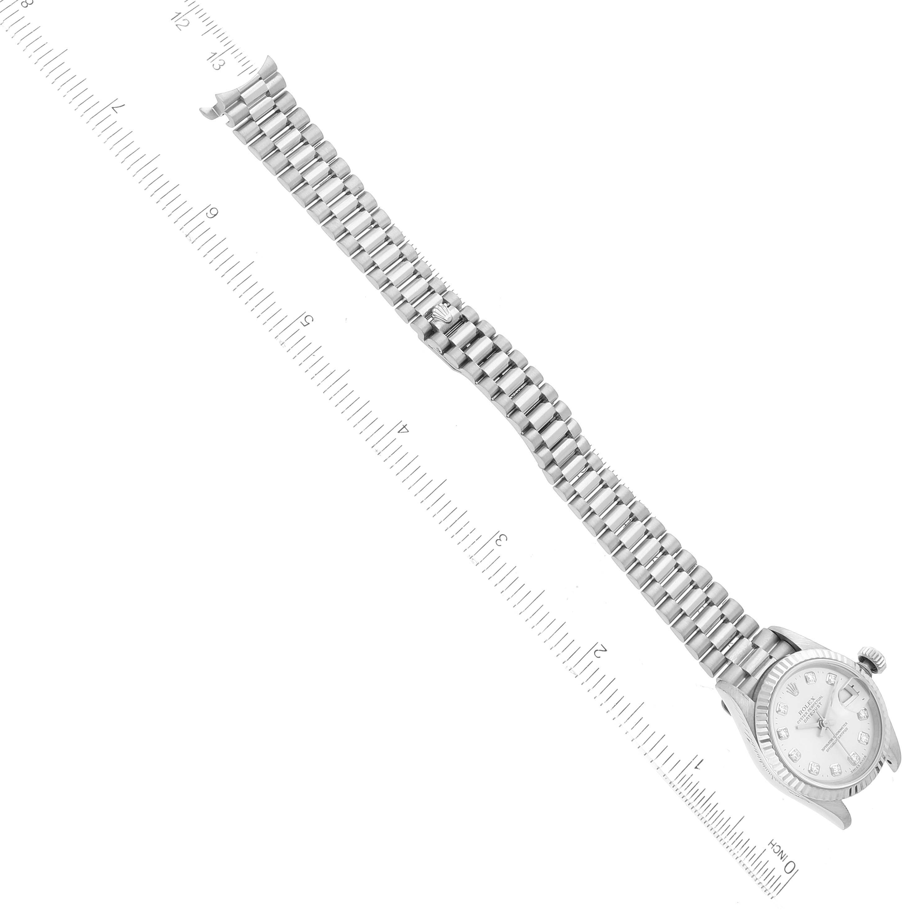 The image shows a Rolex President 69179 Women
s White Gold Silver Dial 69179 Women
s White Gold Silver Dial model watch from a top-down angle, highlighting its face and entire metal bracelet next to a ruler.