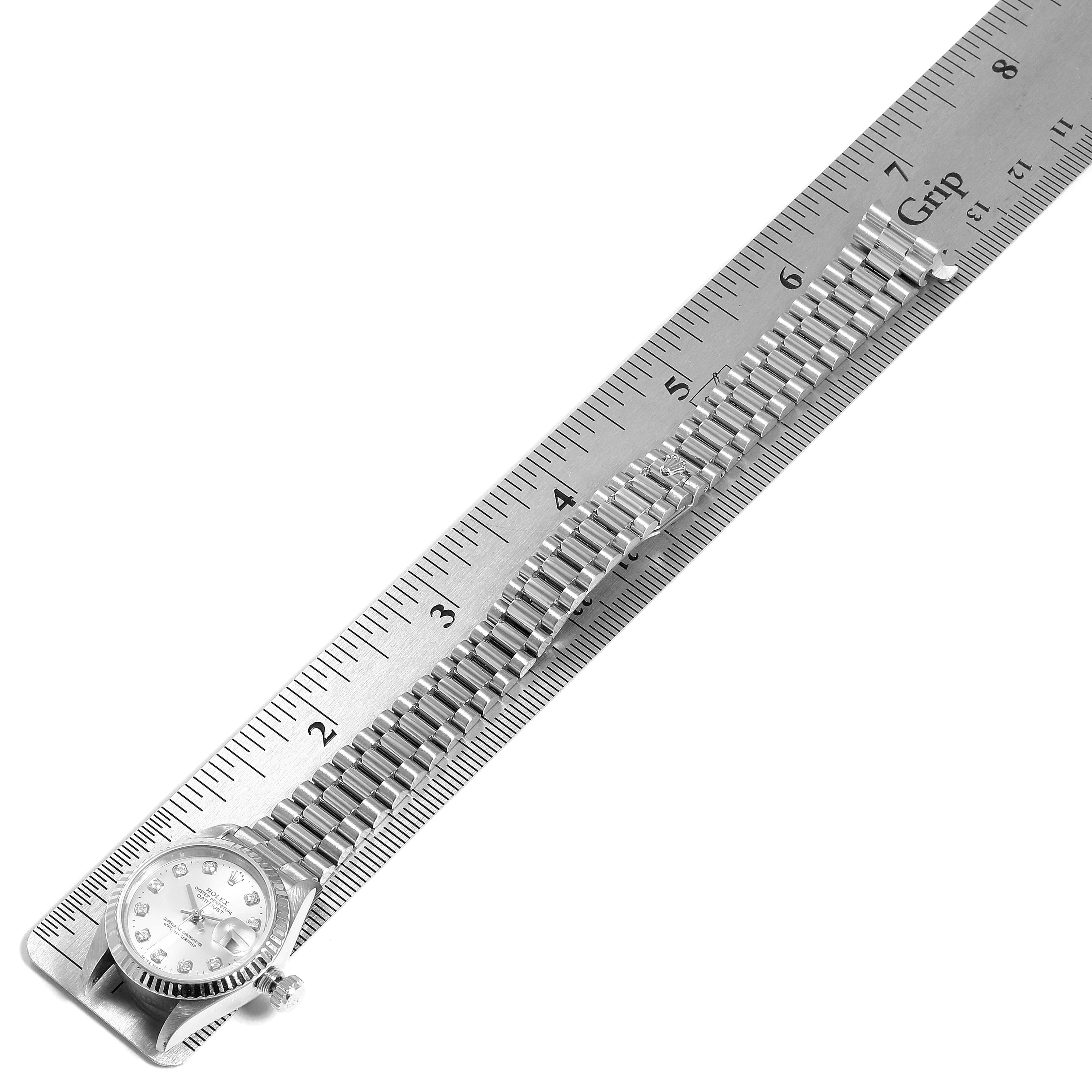 The image shows a Rolex President 69179 Women's White Gold Silver Dial 69179 Women's White Gold Silver Dial model watch laid flat against a ruler, displaying its face and bracelet links.