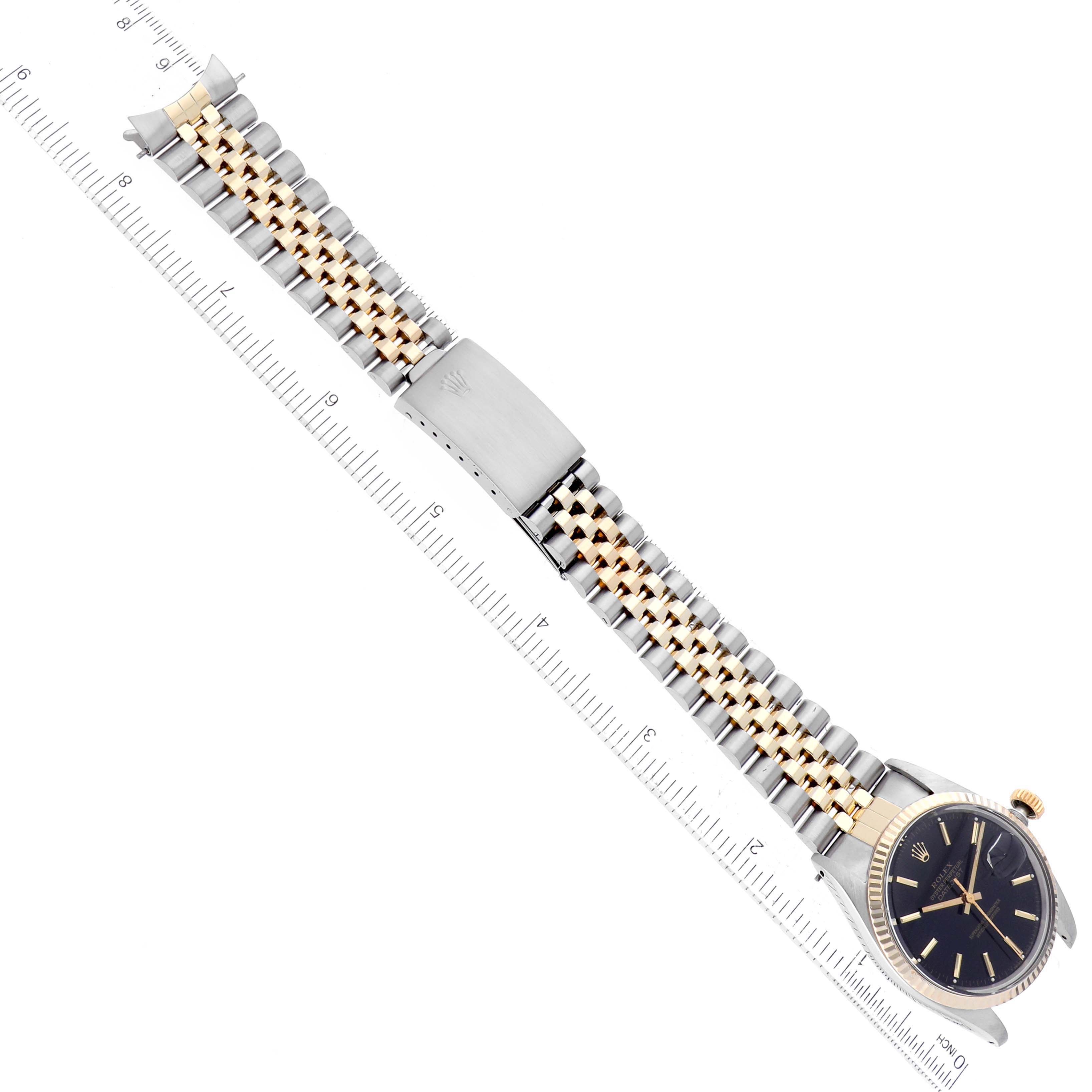 The image shows a Rolex Datejust 16013 Men's Steel and Gold (two tone) Black Dial 16013 Men's Steel and Gold (two tone) Black Dial watch laid flat, displaying its face, bezel, and two-tone bracelet against a ruler.