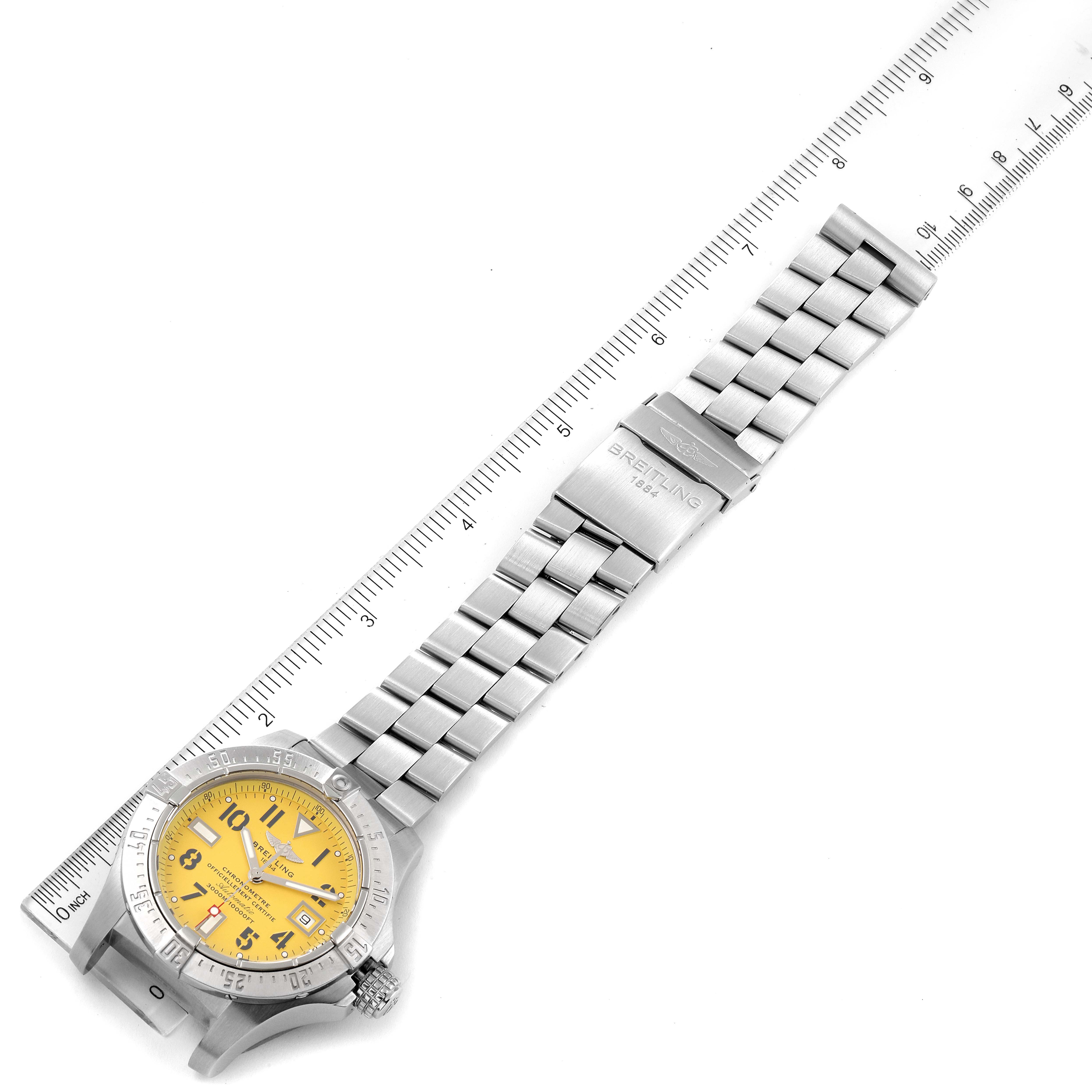 The image shows a top-down angle of a Breitling Avenger A17330 Men's Stainless Steel Yellow Dial A17330 Men's Stainless Steel Yellow Dial watch with a yellow dial and a stainless steel bracelet alongside a ruler.