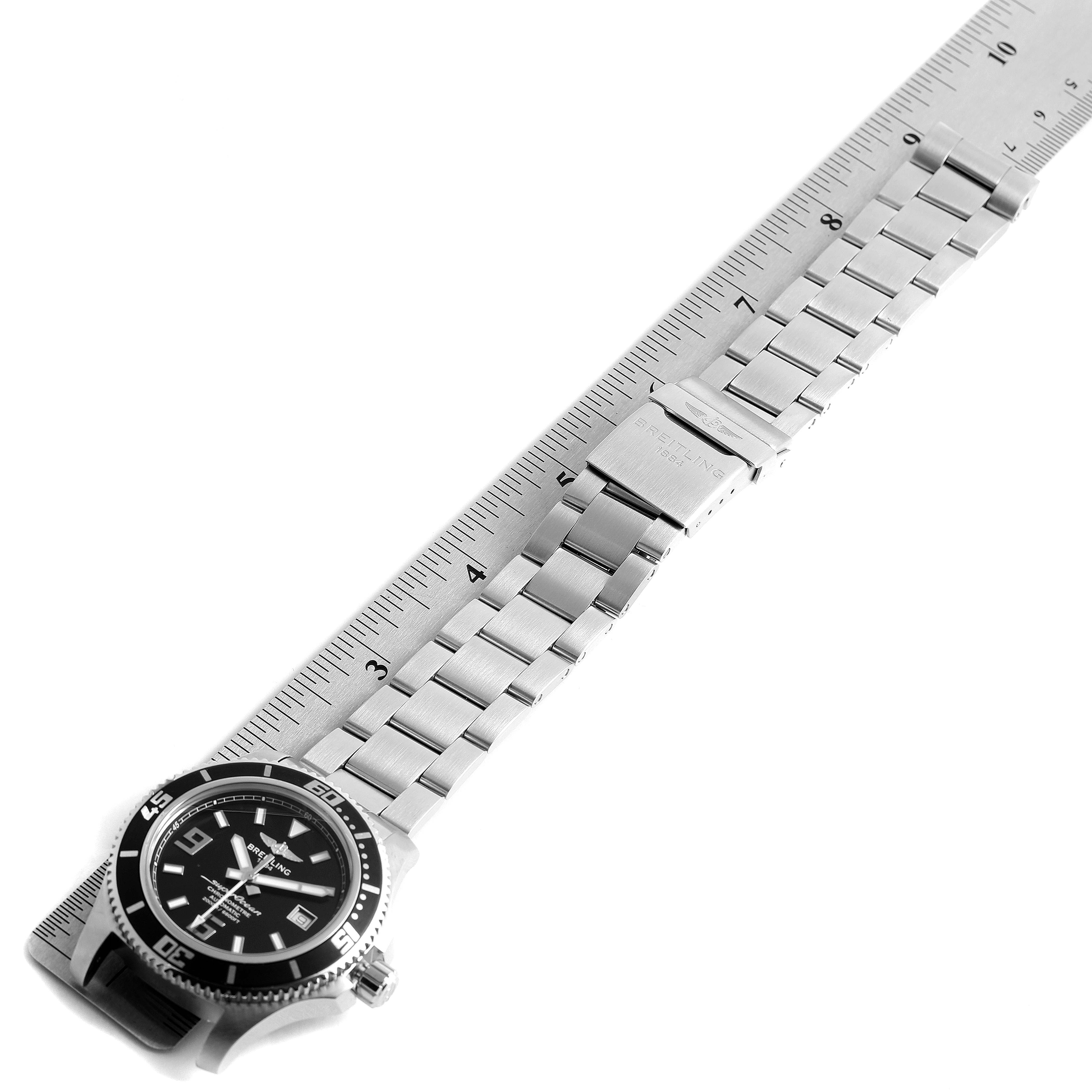 The image shows a Breitling Superocean A17391 Men
s Stainless Steel Black Dial A17391 Men
s Stainless Steel Black Dial watch laid flat, displaying the face and metal bracelet with a ruler for scale.