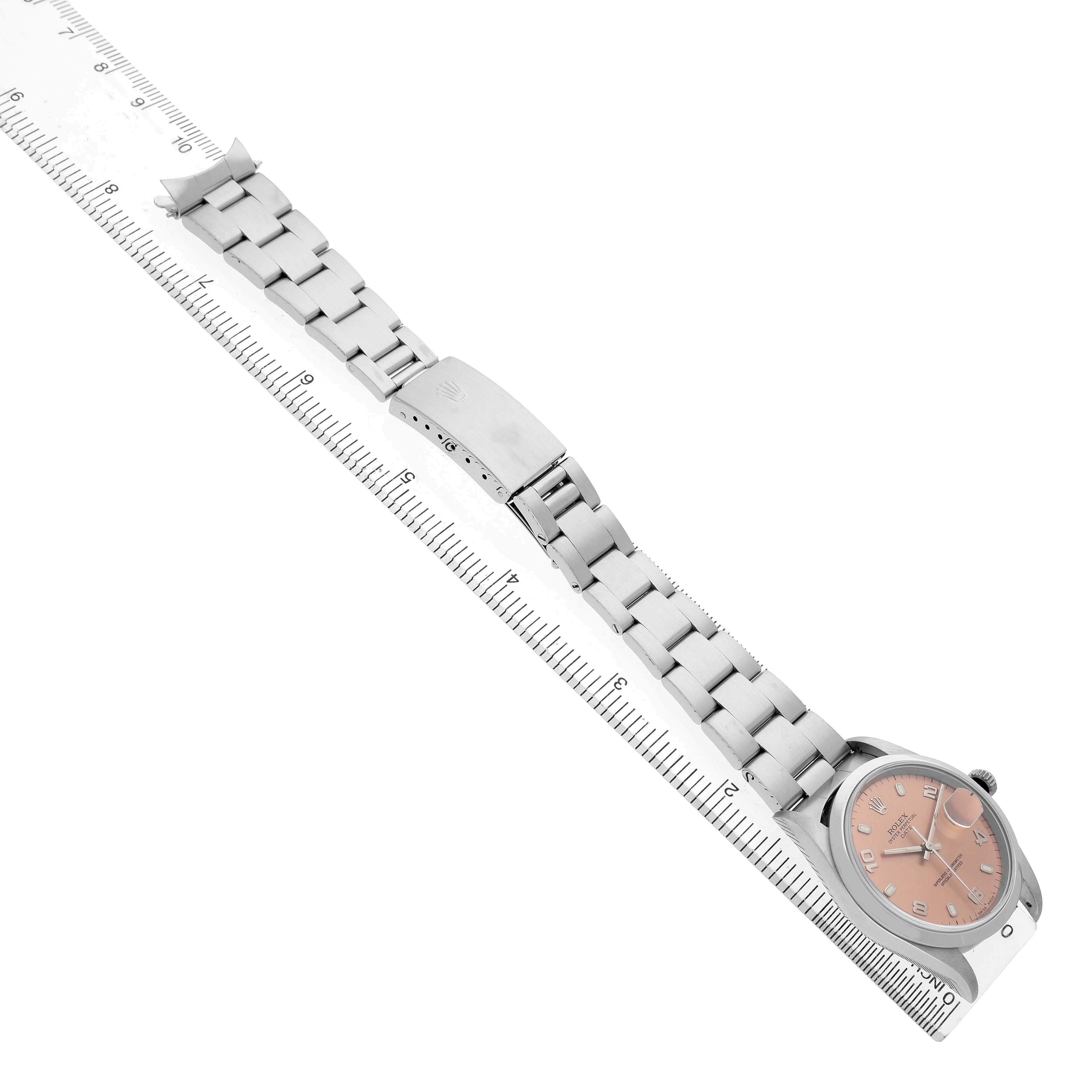 The Rolex Date Men's Stainless Steel Pink Dial watch is shown at an angle, displaying the full bracelet, clasp, and face, alongside a measuring ruler.
