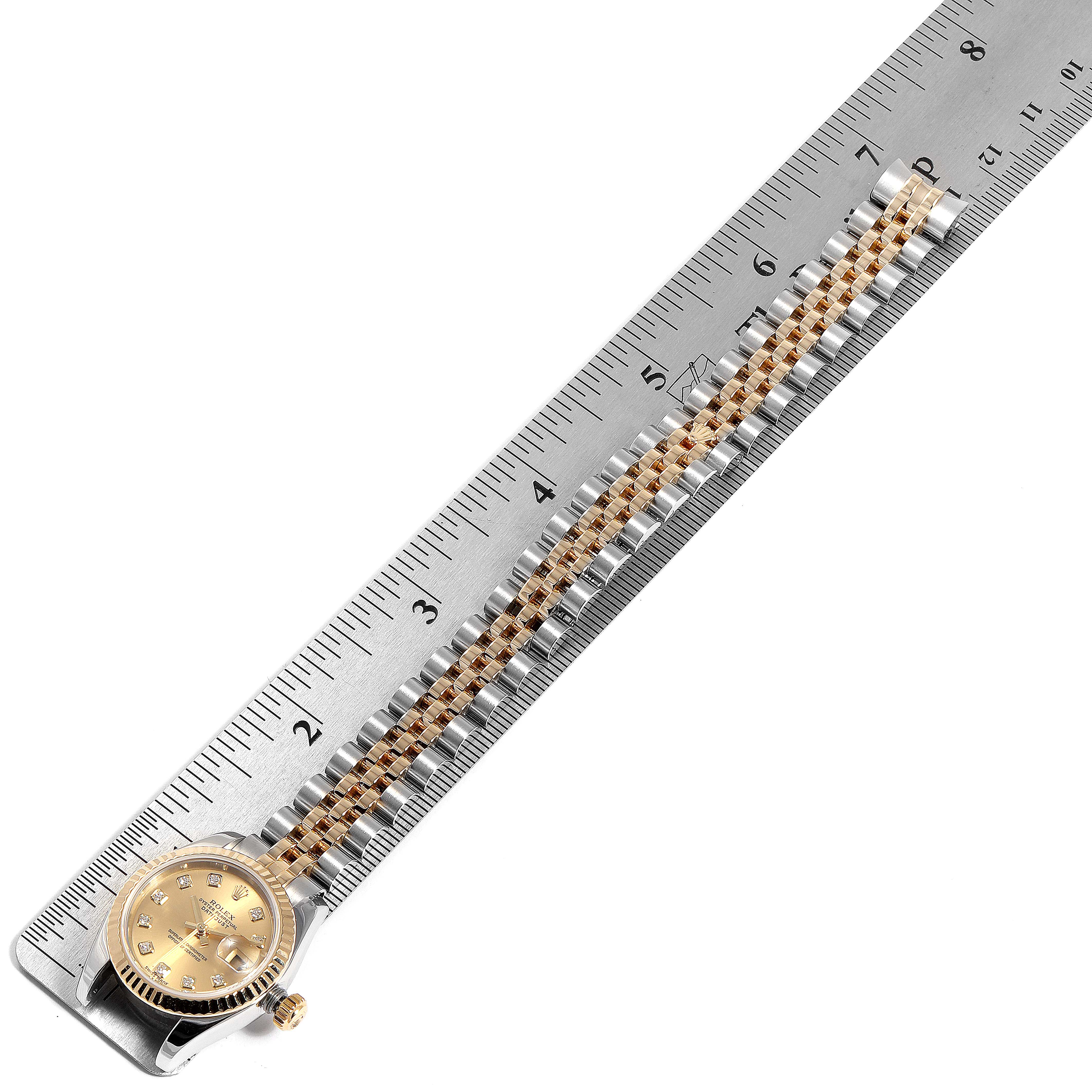 The image shows a Rolex Datejust 179173 Women
s Steel and Gold (two tone) Champagne Dial 179173 Women
s Steel and Gold (two tone) Champagne Dial watch laid next to a ruler for measurement, viewed from above.