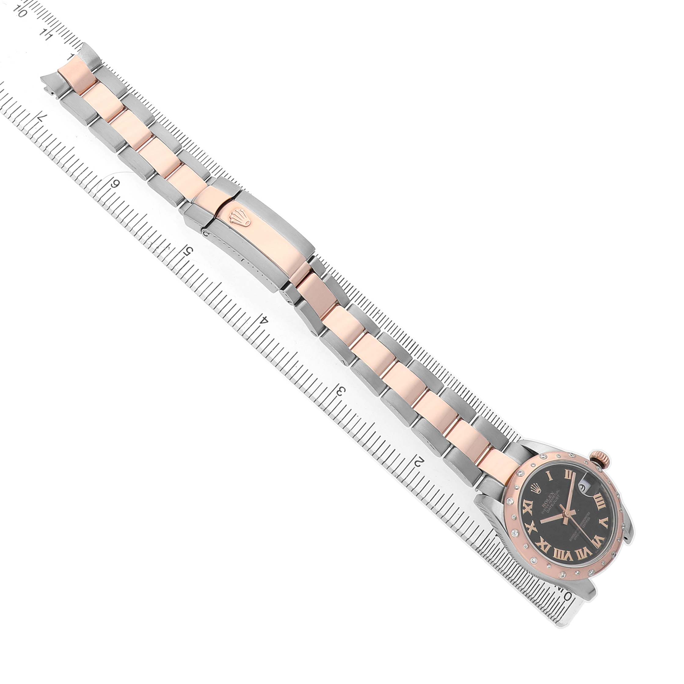 The Rolex Datejust 178341 Women's Steel and Gold (two tone) Black Dial watch is shown from a top-down angle, highlighting its bracelet, clasp, and face placed along a ruler.