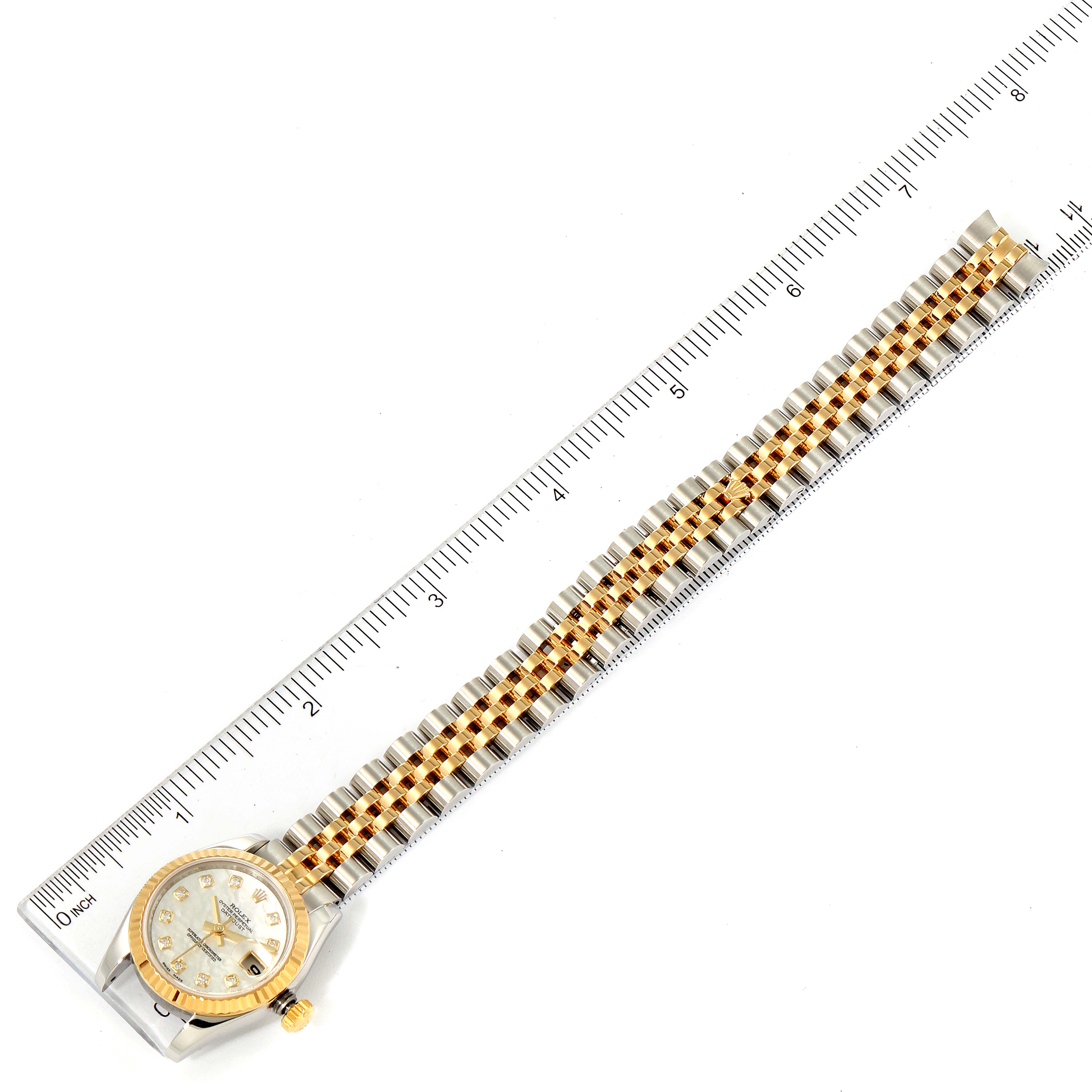 The Rolex Datejust 179173 Women's Steel and Gold (two tone) Mother of Pearl Dial 179173 Women's Steel and Gold (two tone) Mother of Pearl Dial watch is shown from a top-down angle, displaying its face and two-tone bracelet alongside a ruler.