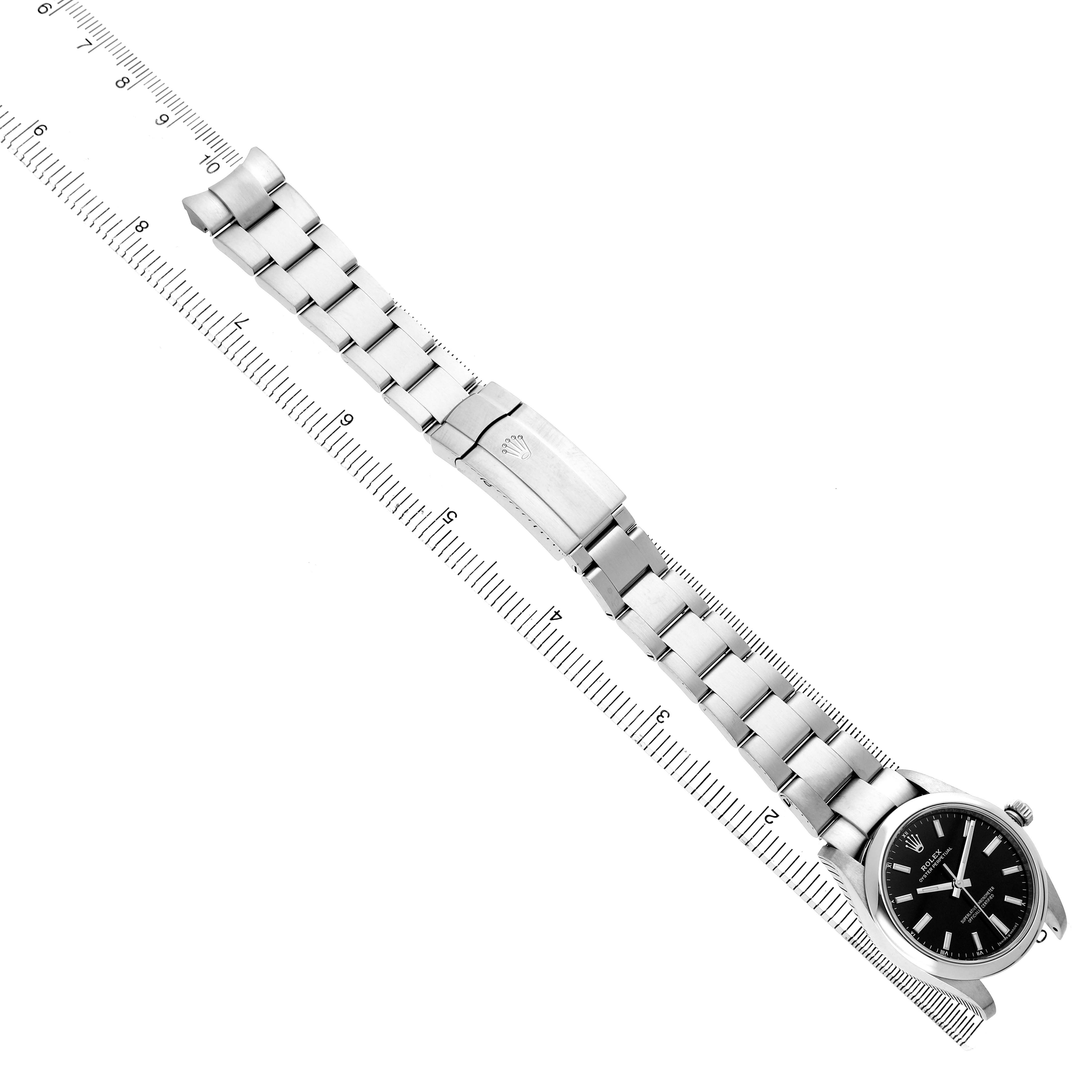 The Rolex Oyster Perpetual 124200 Men's Stainless Steel Black Dial watch is shown laid flat, displaying the watch face, bracelet, and clasp from a top-down angle alongside a ruler.