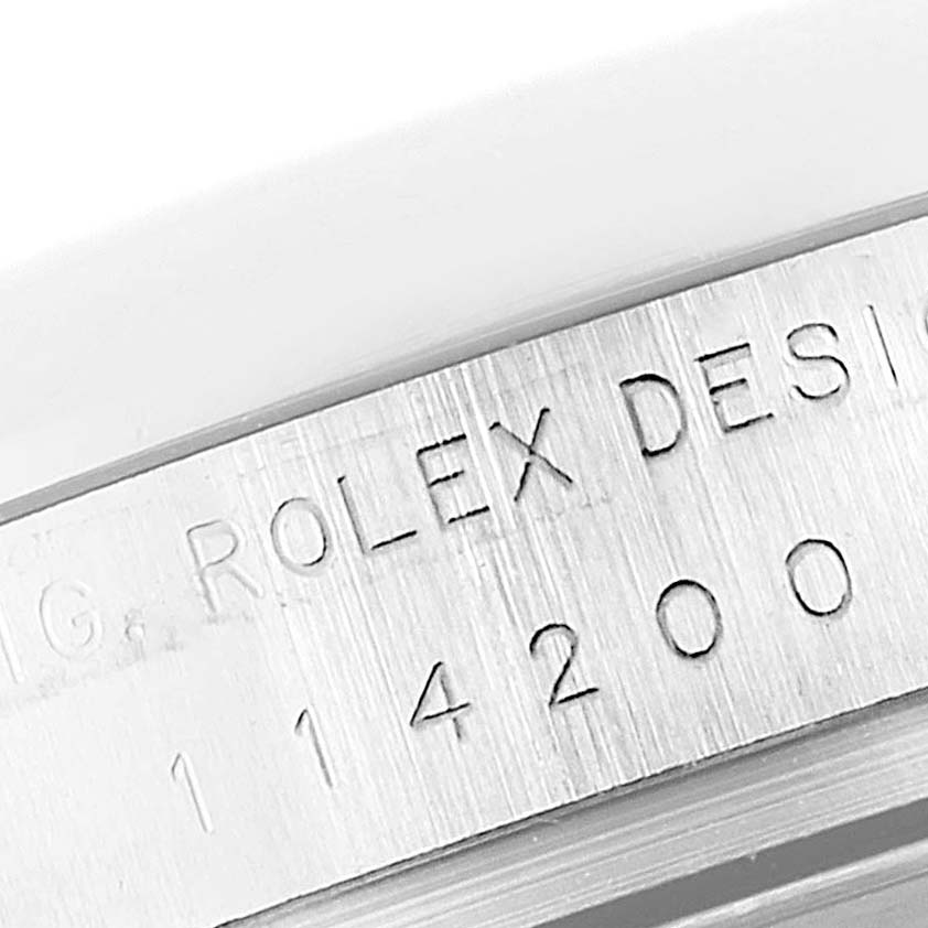The image shows a close-up of the engraved serial number on the side of the Rolex Oyster Perpetual 114200 Men's Stainless Steel Green Dial 114200 Men's Stainless Steel Green Dial watch case.