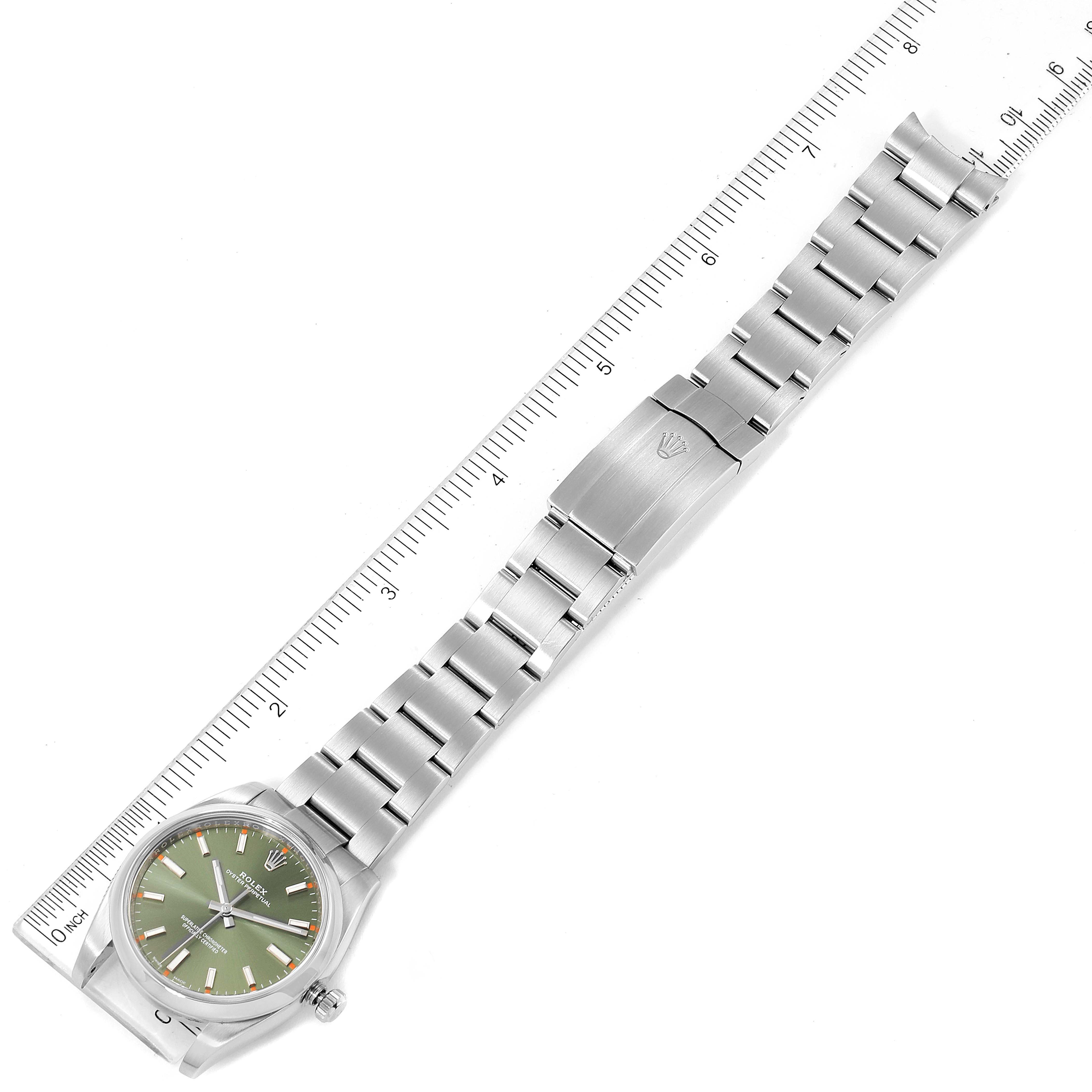 The image shows a top-down view of a Rolex Oyster Perpetual 114200 Men's Stainless Steel Green Dial 114200 Men's Stainless Steel Green Dial watch, showcasing the face, band, and clasp next to a ruler.