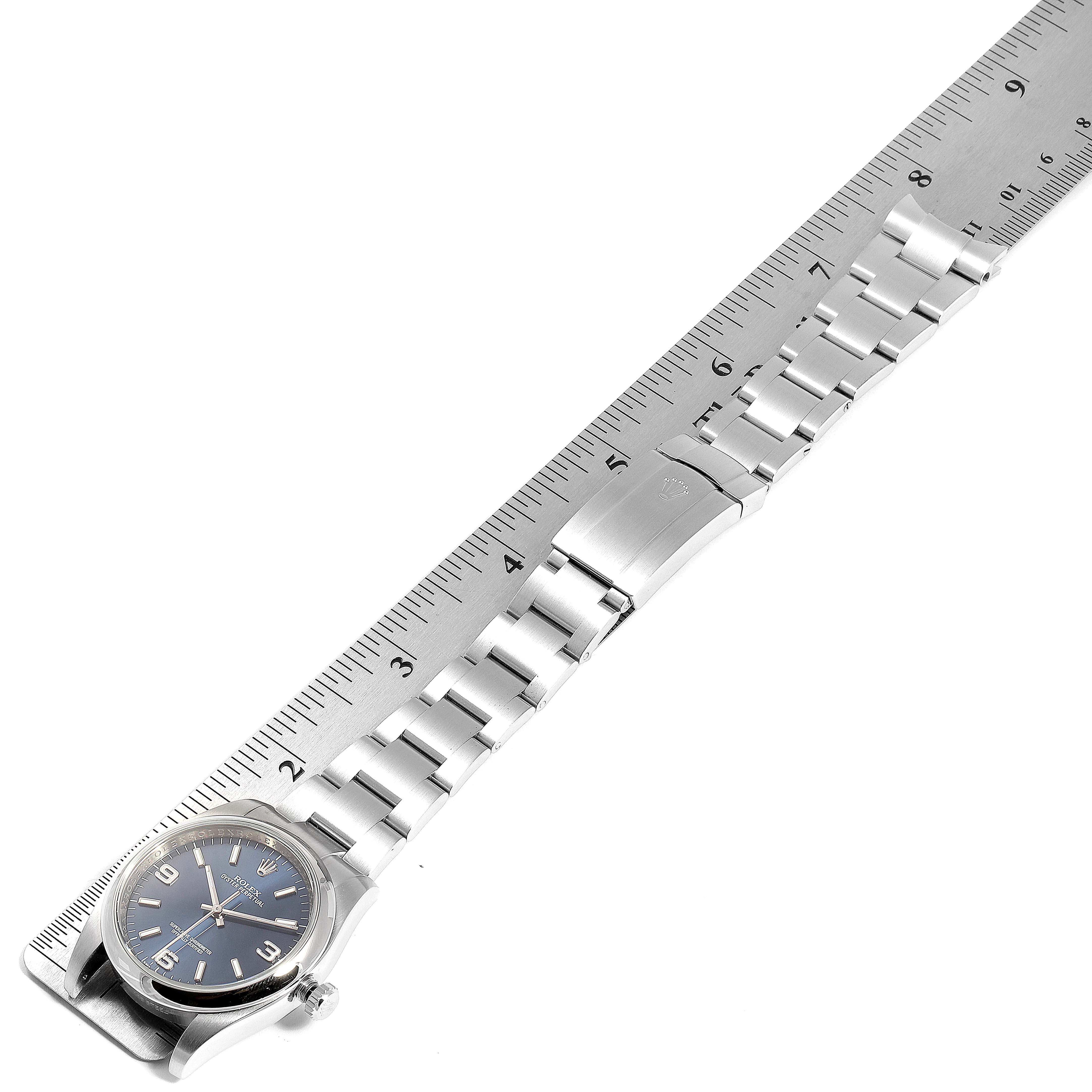 The image shows a Rolex Oyster Perpetual 116000 Men's Stainless Steel Blue Dial 116000 Men's Stainless Steel Blue Dial watch with a metallic strap and a ruler next to it for measurement.