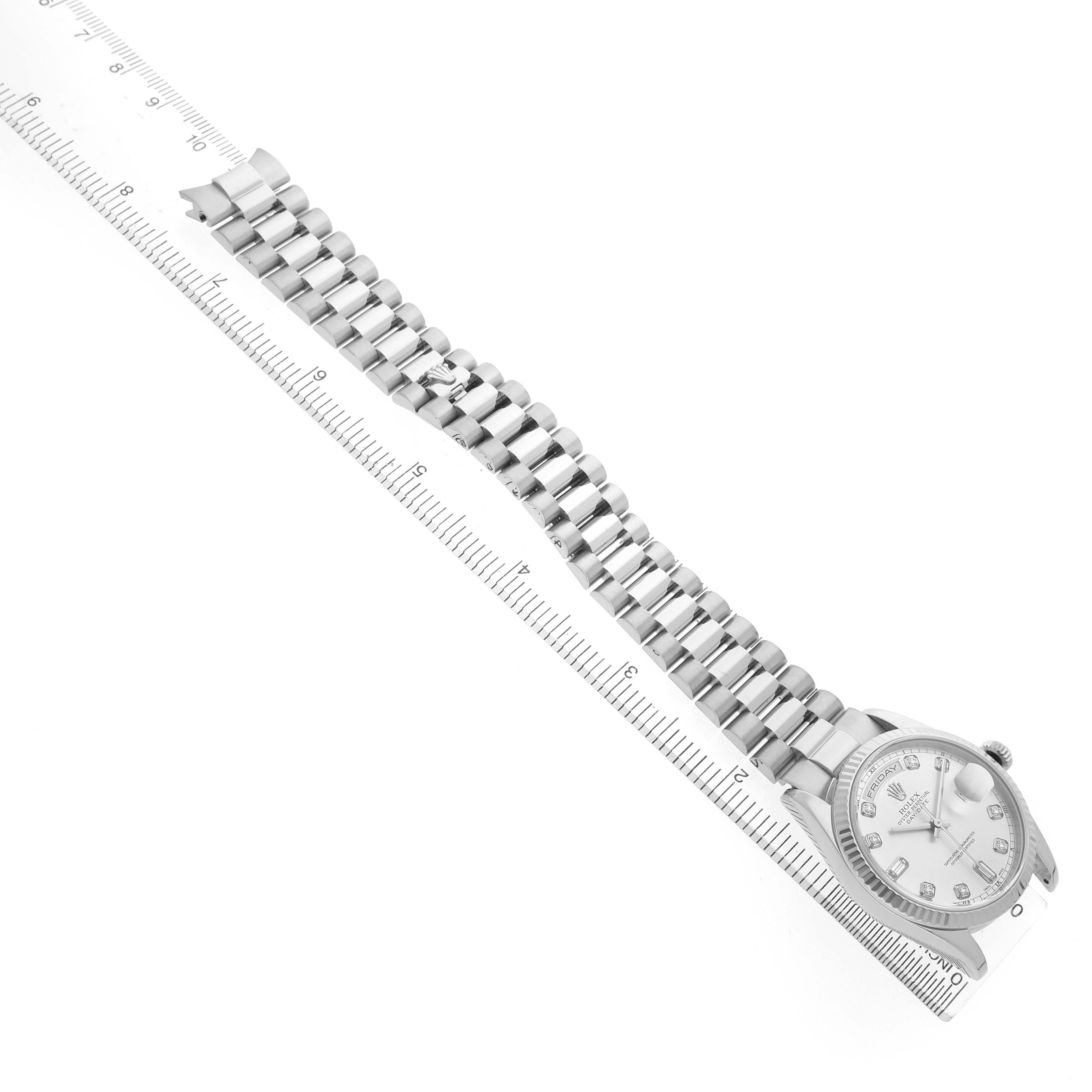 The Rolex President 118239 Men's White Gold Silver Dial model watch is shown from a top-down angle, highlighting its face and bracelet alongside a ruler for scale.