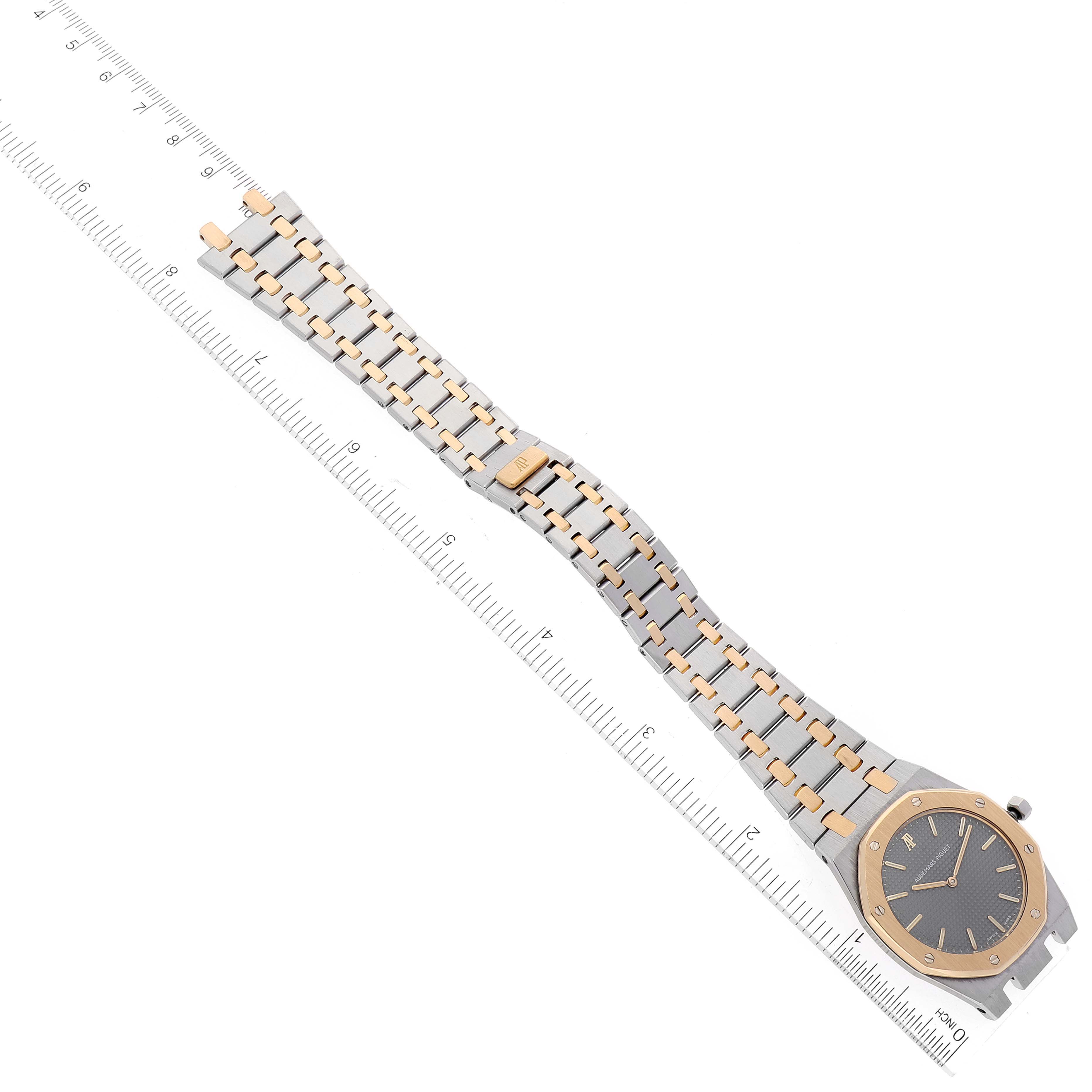 The image shows an Audemars Piguet Royal Oak 56303SA Men
s Steel and Gold (two tone) Grey Dial 56303SA Men
s Steel and Gold (two tone) Grey Dial watch laid flat beside a ruler, highlighting the bracelet and face.