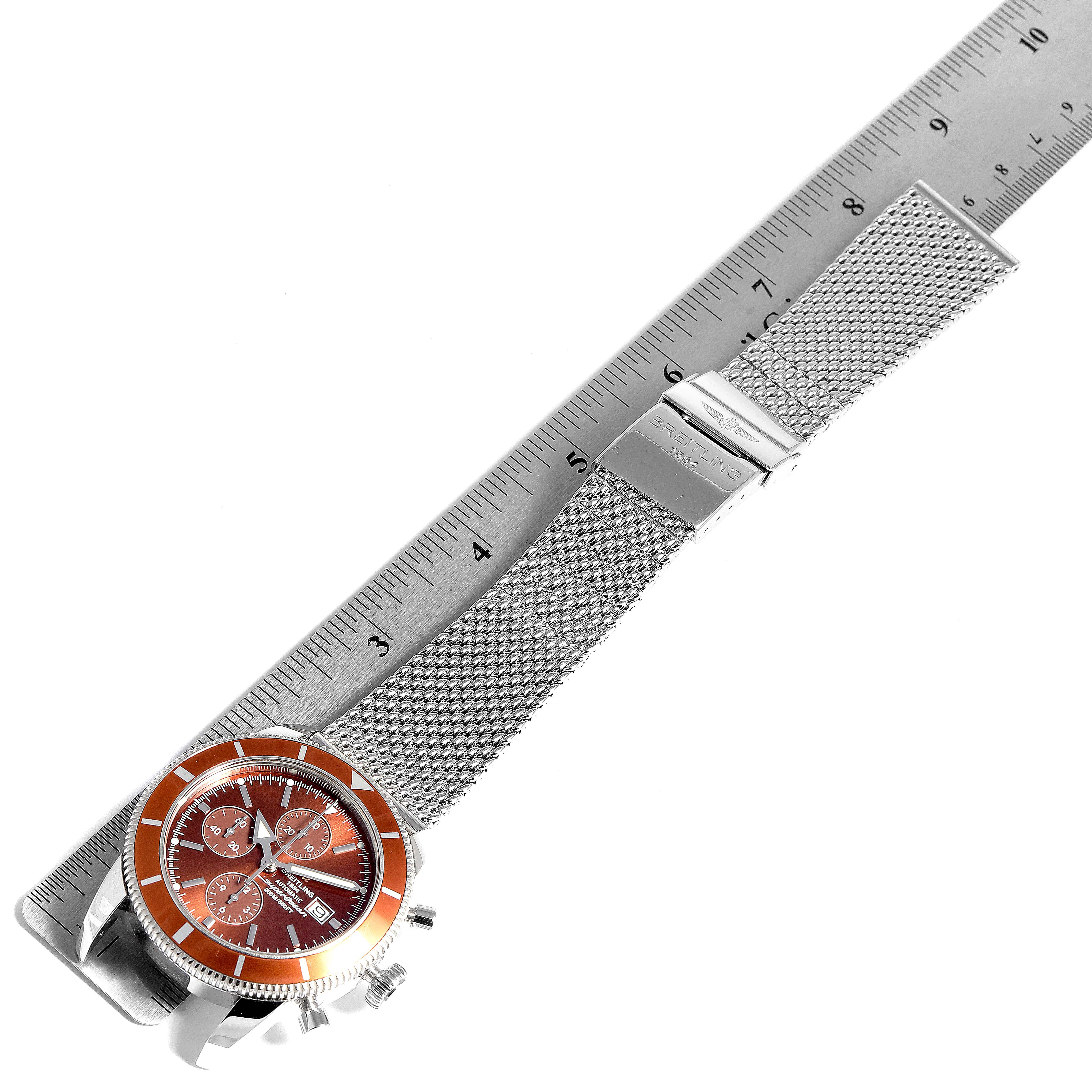 The image shows a top-down view of a Breitling Superocean A13320 Men
s Stainless Steel Brown Dial A13320 Men
s Stainless Steel Brown Dial watch with an orange bezel and stainless steel mesh strap, alongside a ruler for scale.