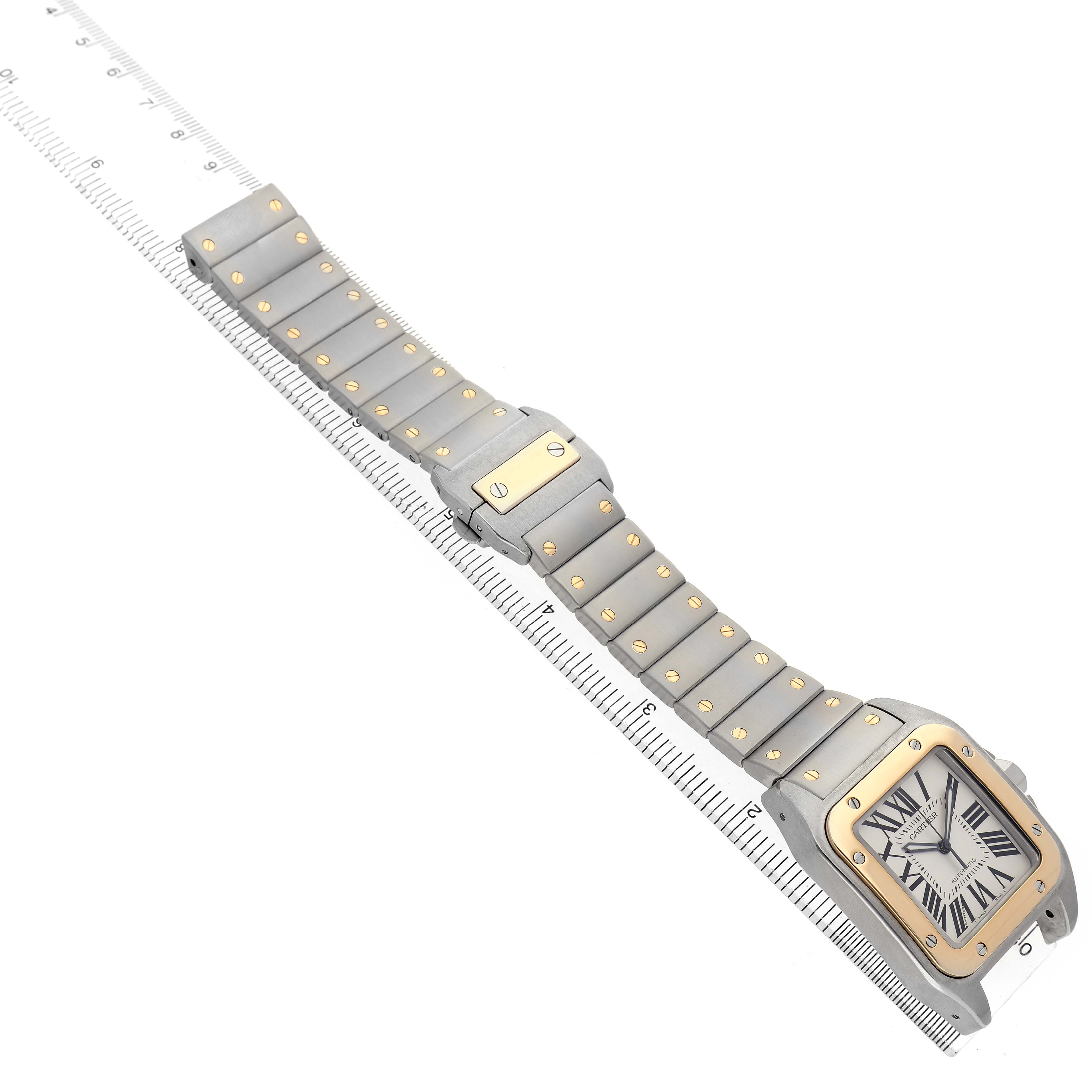 The Santos by Cartier watch is shown at a diagonal angle, highlighting its face, bezel, and full metal bracelet against a ruler.