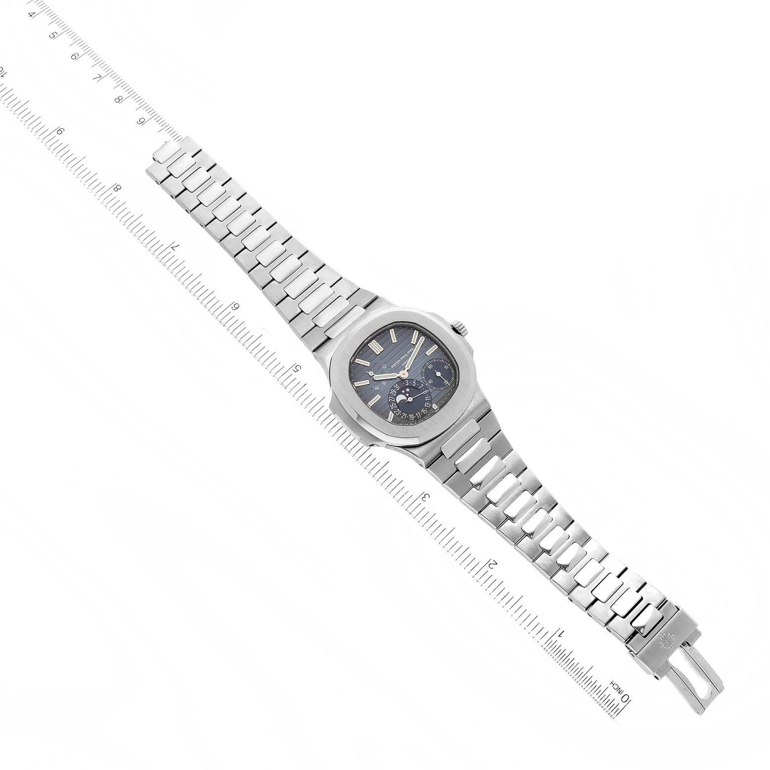 The image shows a Patek Philippe Nautilus 5712/1A-001 Men
s Stainless Steel Blue Dial 5712/1A-001 Men
s Stainless Steel Blue Dial watch laid flat with its face and stainless steel bracelet fully visible next to a ruler for scale.