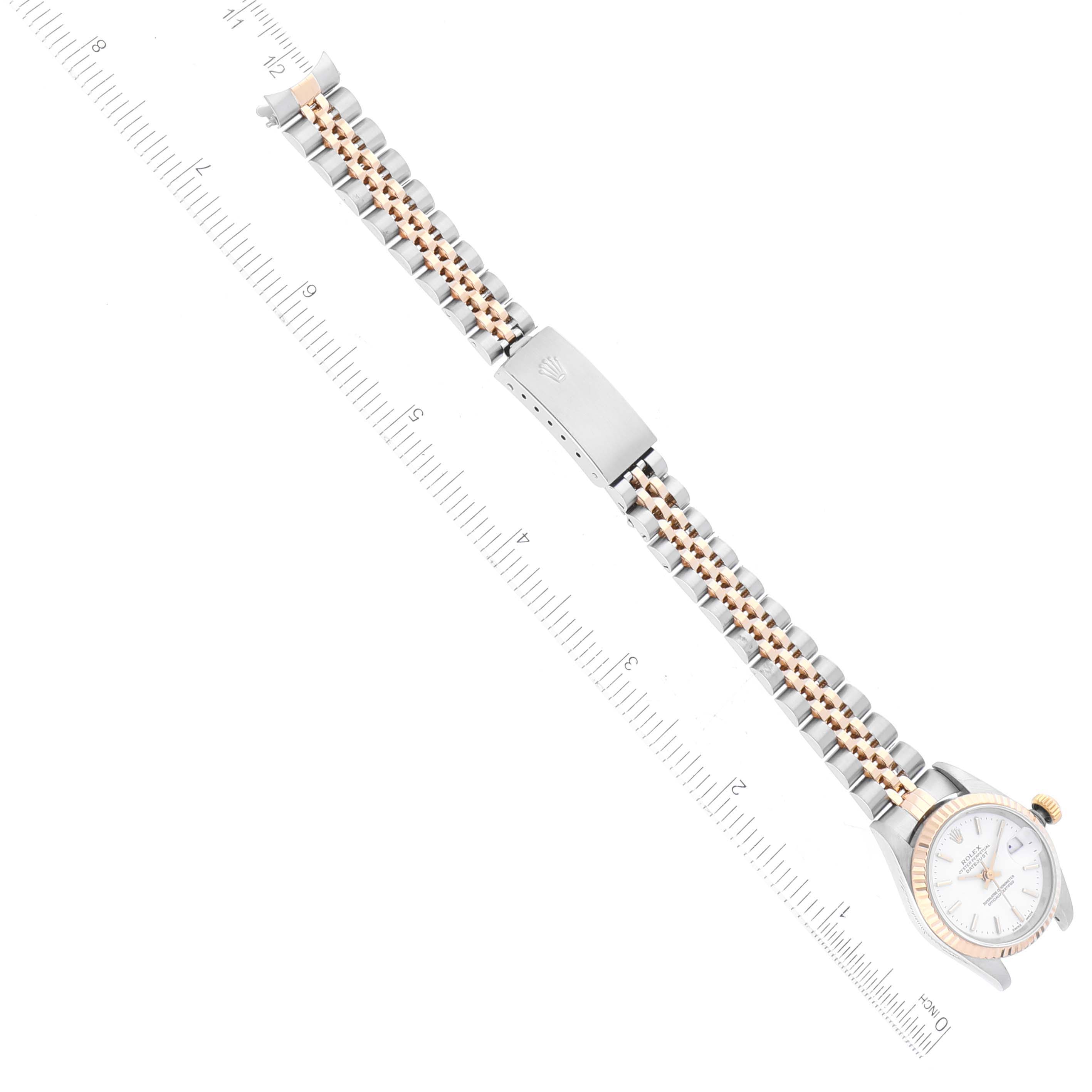 The image shows a top-down view of a Rolex Datejust 79173 Women's Steel and Gold (two tone) White Dial 79173 Women's Steel and Gold (two tone) White Dial watch, highlighting its band and clasp, alongside a measuring ruler.