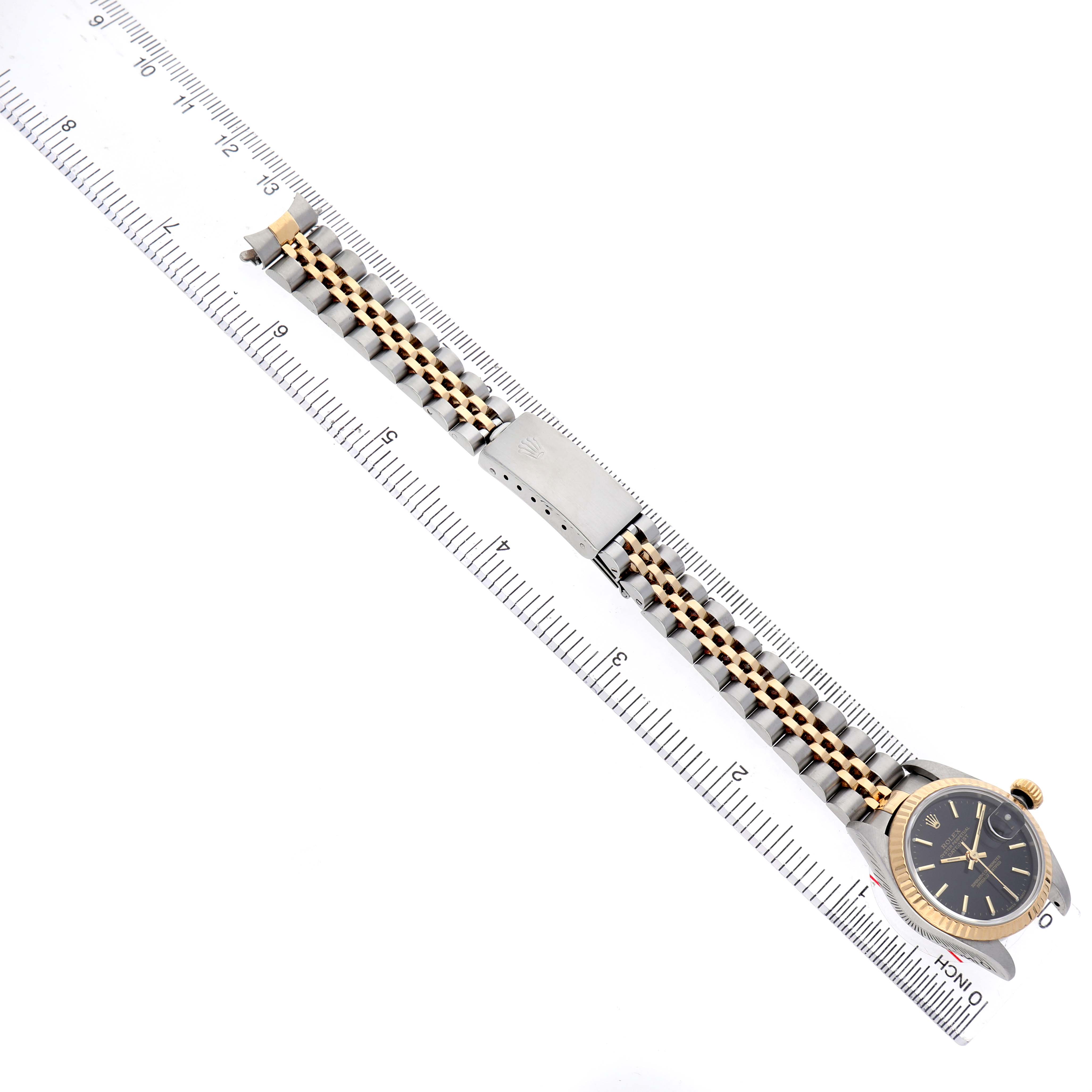 The image shows a Rolex Datejust 79173 Women's Steel and Gold (two tone) Black Dial watch from a top-down angle, displaying its watch face, bezel, and dual-tone bracelet alongside a ruler.