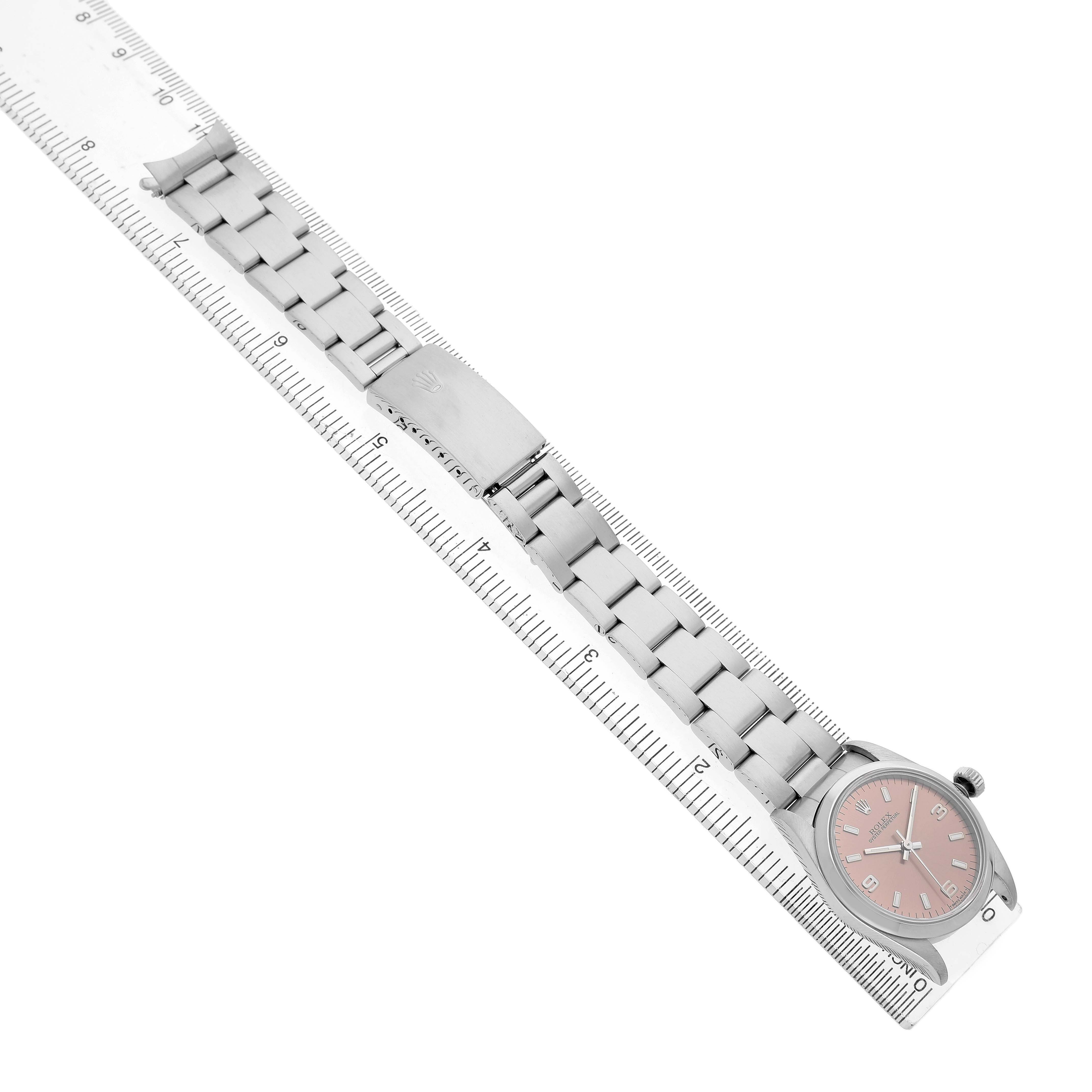 The Rolex Oyster Perpetual 67480 Women's Stainless Steel Pink Dial watch is shown from an overhead angle, displaying its bracelet, clasp, and dial alongside a ruler.