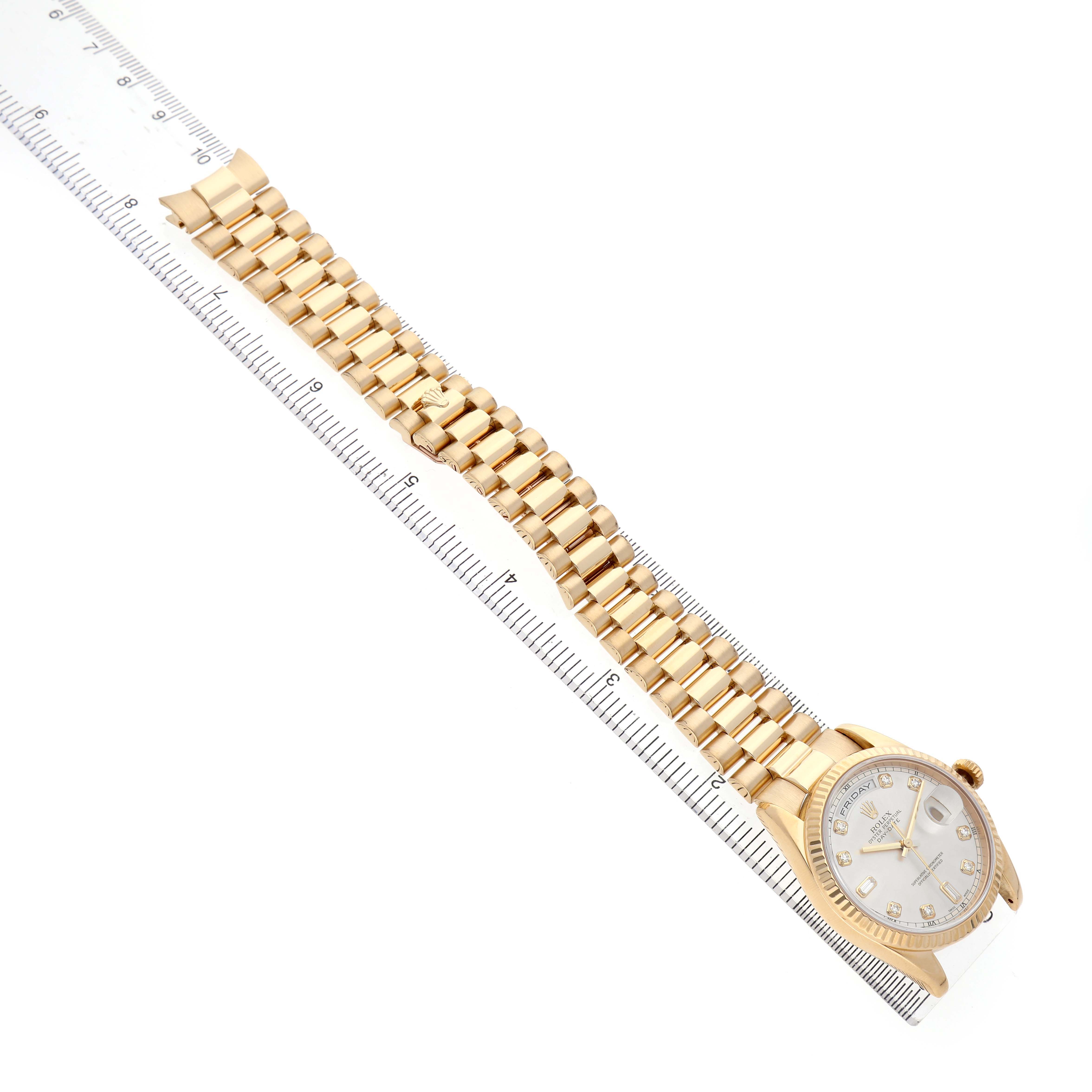 The Rolex President 36 Men's Yellow Gold Silver Dial model is shown from a top-down angle, revealing the watch face, bezel, and full bracelet beside a ruler.