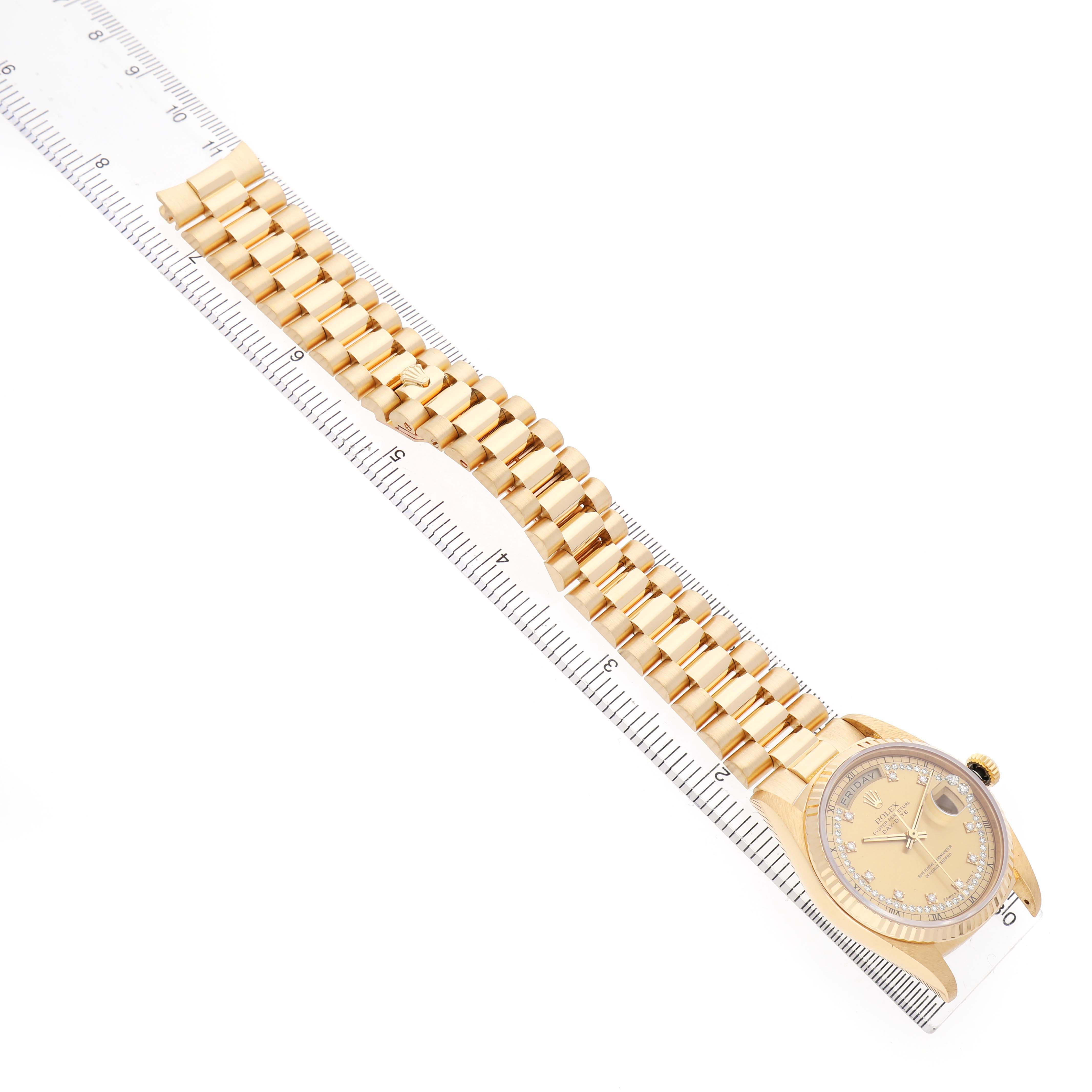 The Rolex President 18238 Men's Yellow Gold Champagne Dial model watch is shown from a top-down angle, displaying the dial and gold bracelet along a ruler.