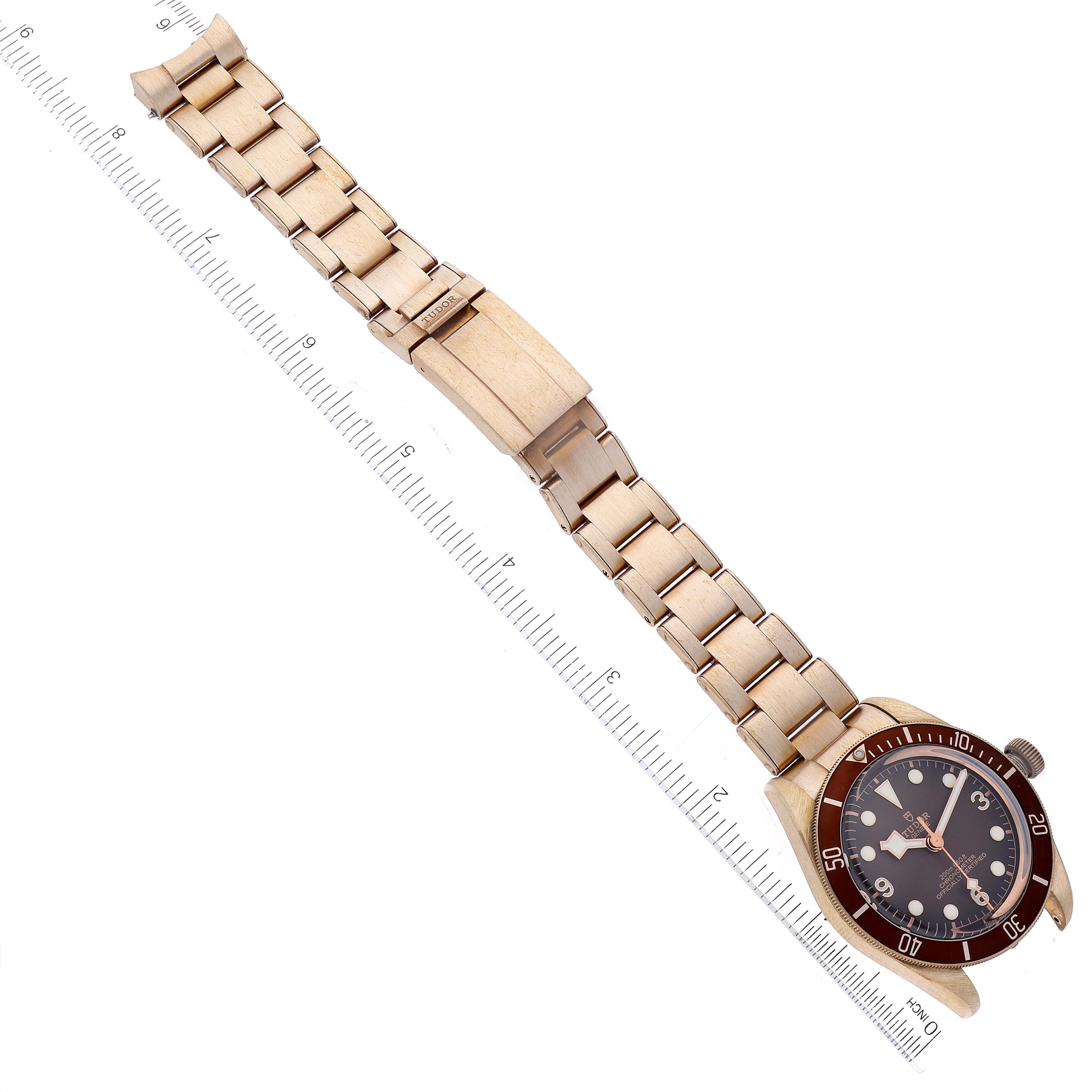 The image shows a Tudor Heritage Black Bay 79012 Men's Bronze Brown Dial 79012 Men's Bronze Brown Dial watch laid flat alongside a ruler, displaying its bracelet and clasp.