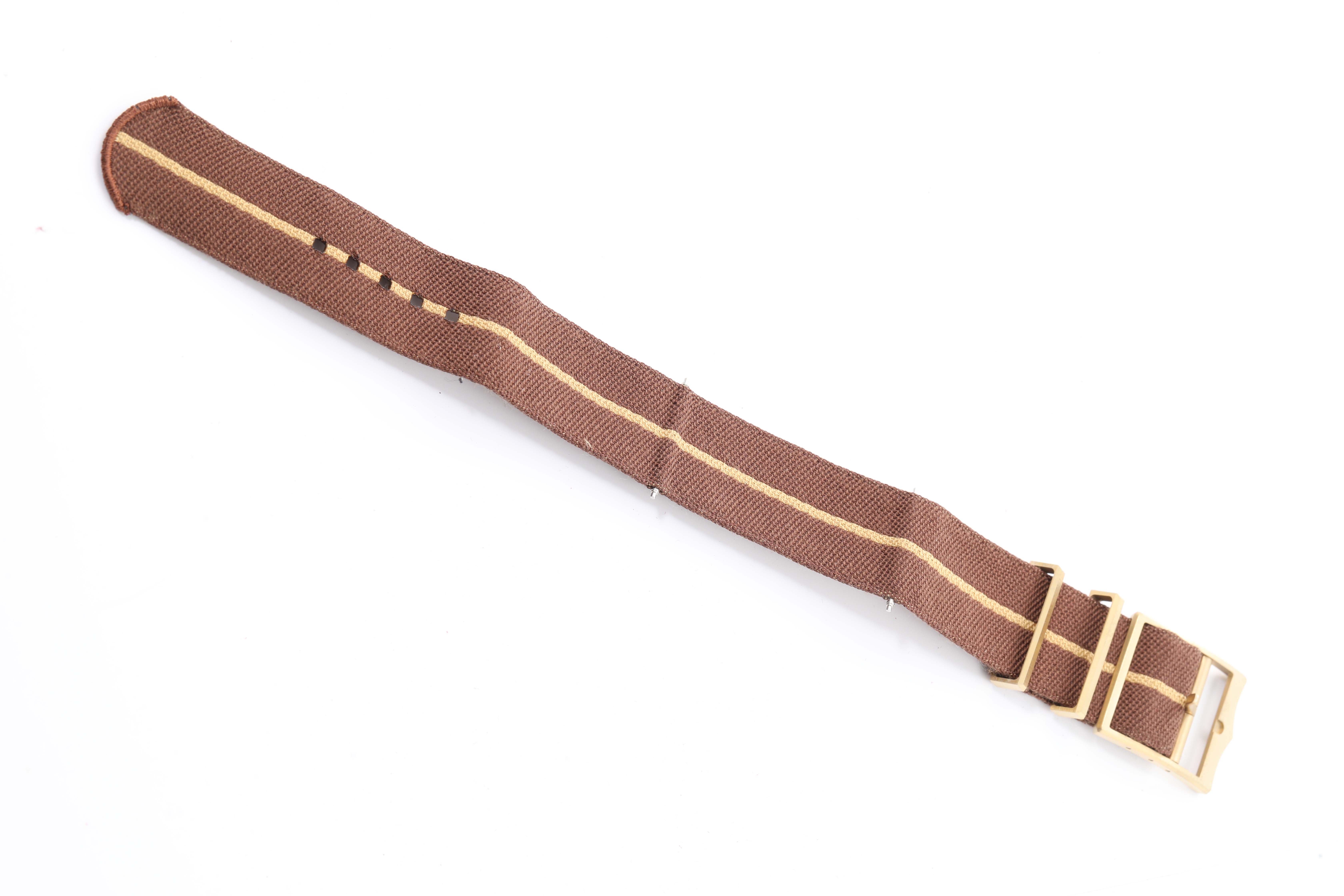 This image shows a brown fabric strap with brass hardware for the Tudor Heritage Black Bay 79012 Men's Bronze Brown Dial 79012 Men's Bronze Brown Dial watch.