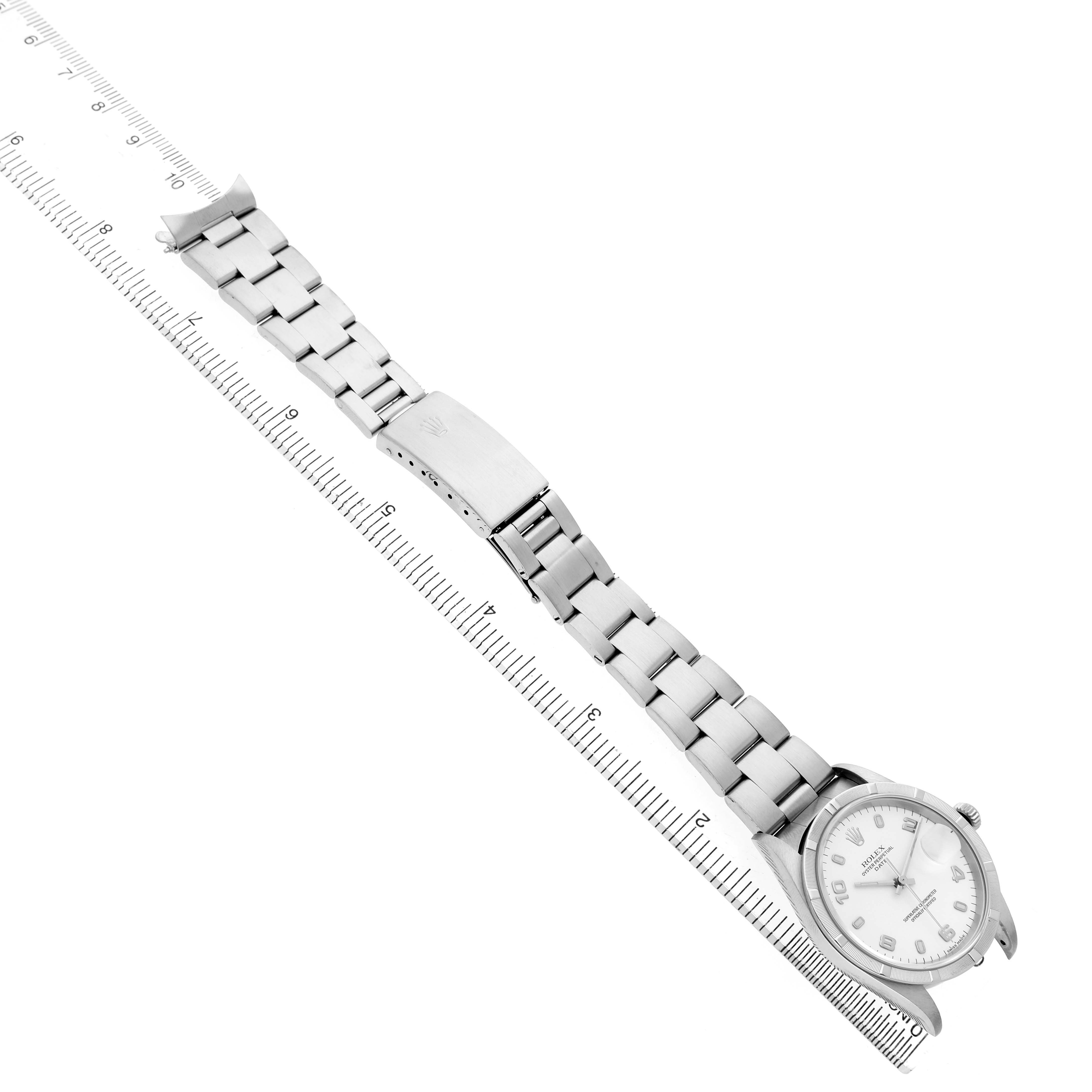 The Rolex Date 15210 Men's Stainless Steel White Dial watch is shown flat, highlighting the face, bracelet, and clasp, alongside a ruler for scale.