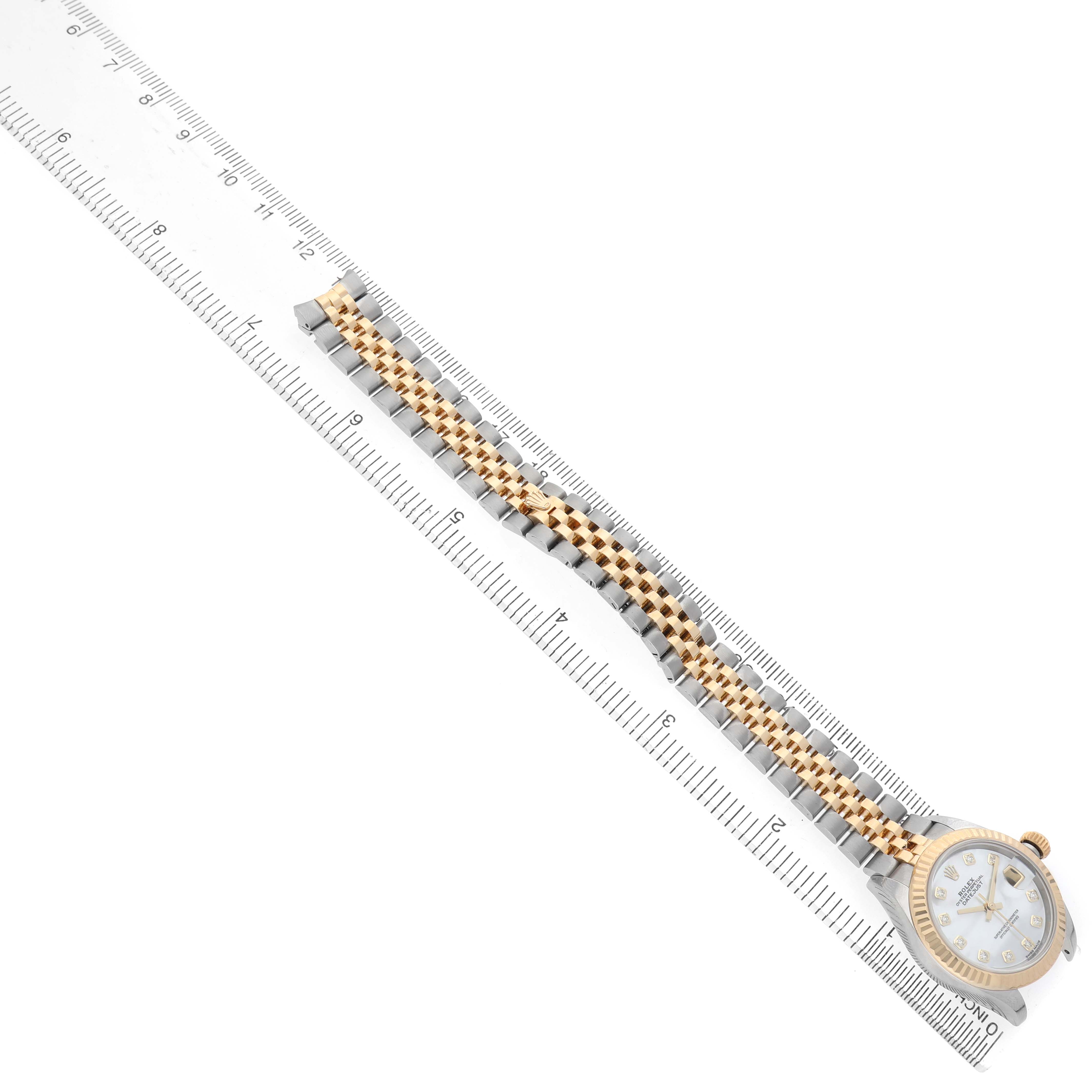 The Rolex Datejust 279173 Women's Steel and Gold (two tone) Mother of Pearl Dial is shown from a top view, highlighting the face and two-tone bracelet alongside a ruler for scale.