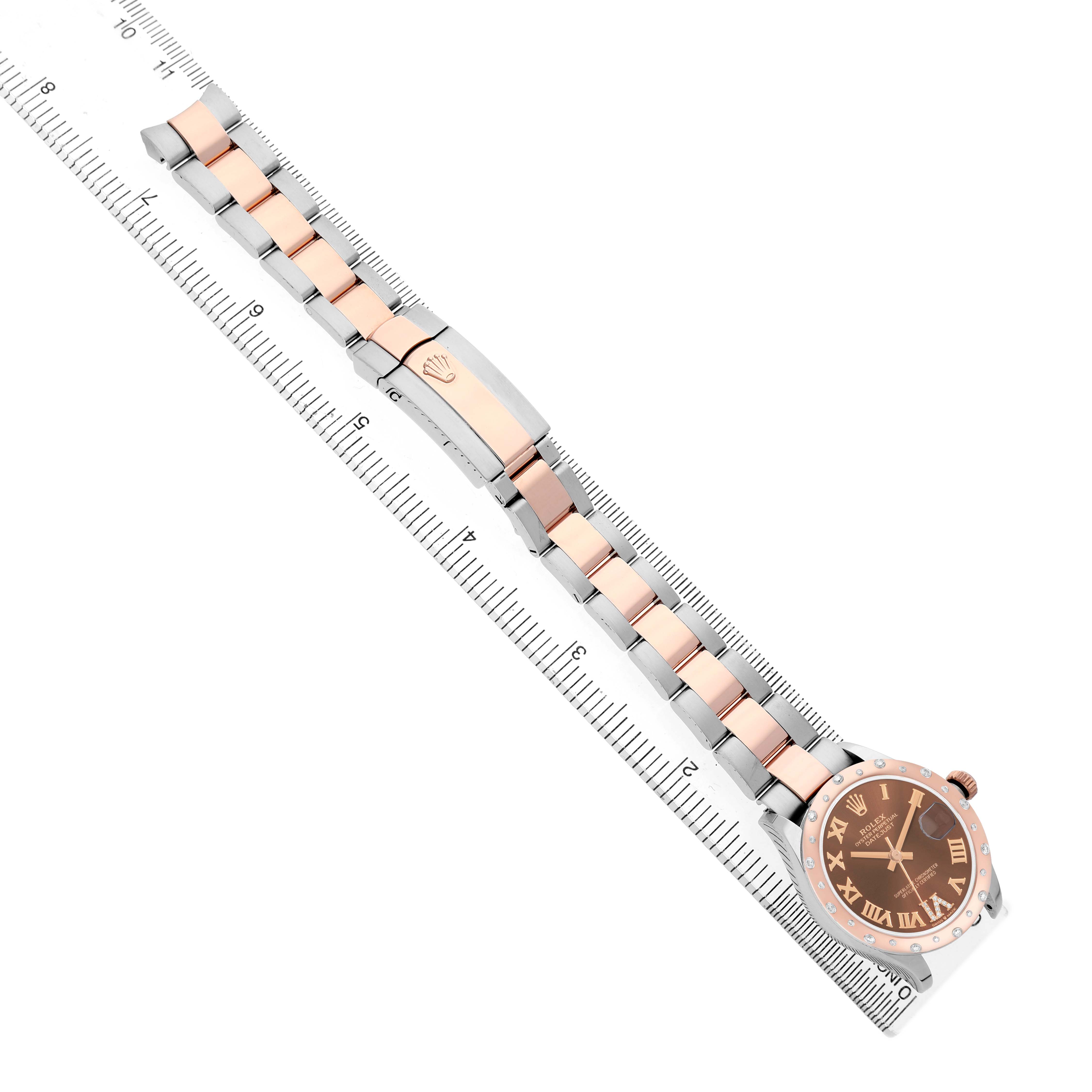The Rolex Datejust 278341 Women's Steel and Gold (two tone) Brown Dial watch is shown from a top-down angle, highlighting the bracelet, clasp, and dial alongside a ruler.