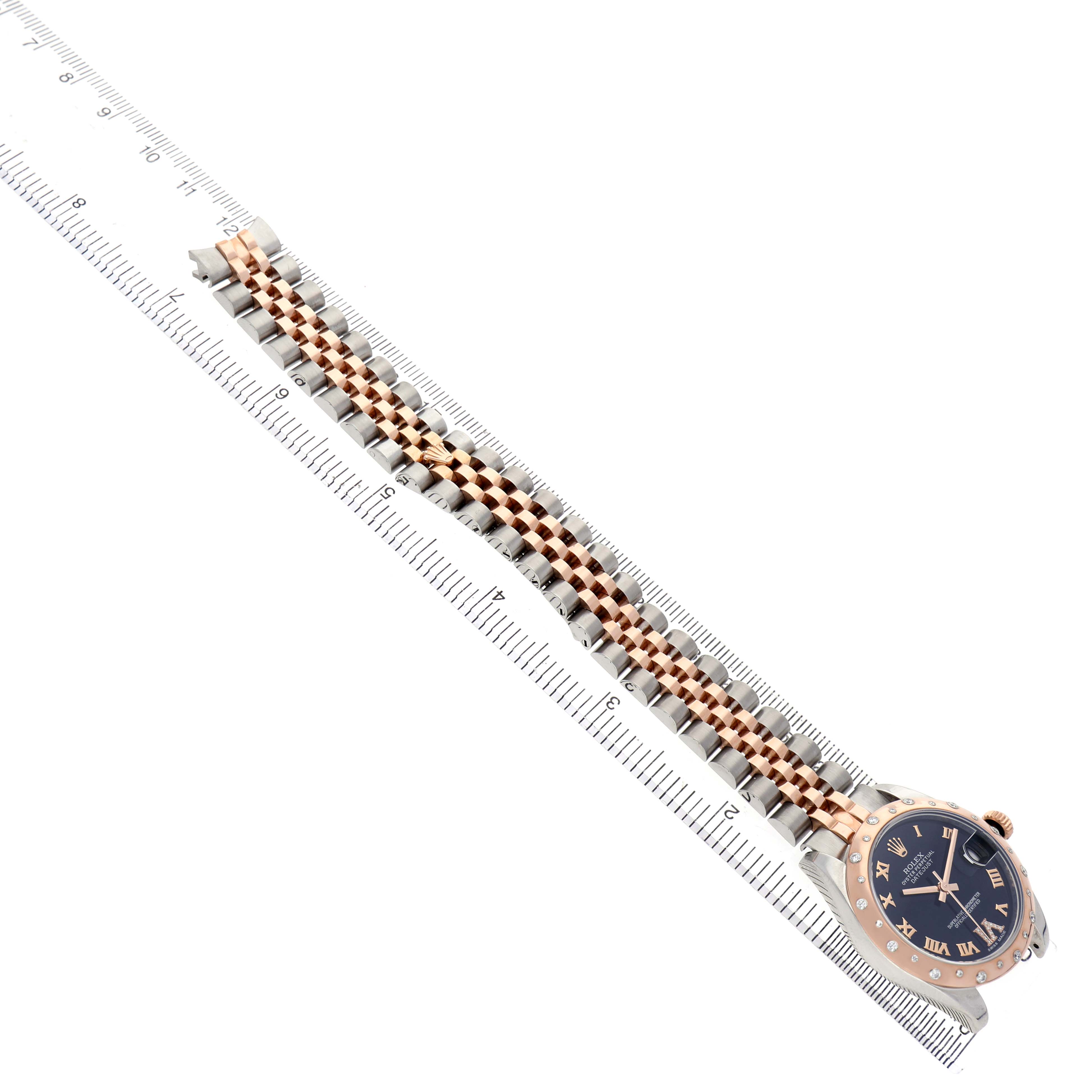 The Rolex Datejust 178341 Women's Steel and Gold (two tone) Black Dial watch is shown at an angle displaying its face, bracelet, and part of the bezel, with a ruler for scale.