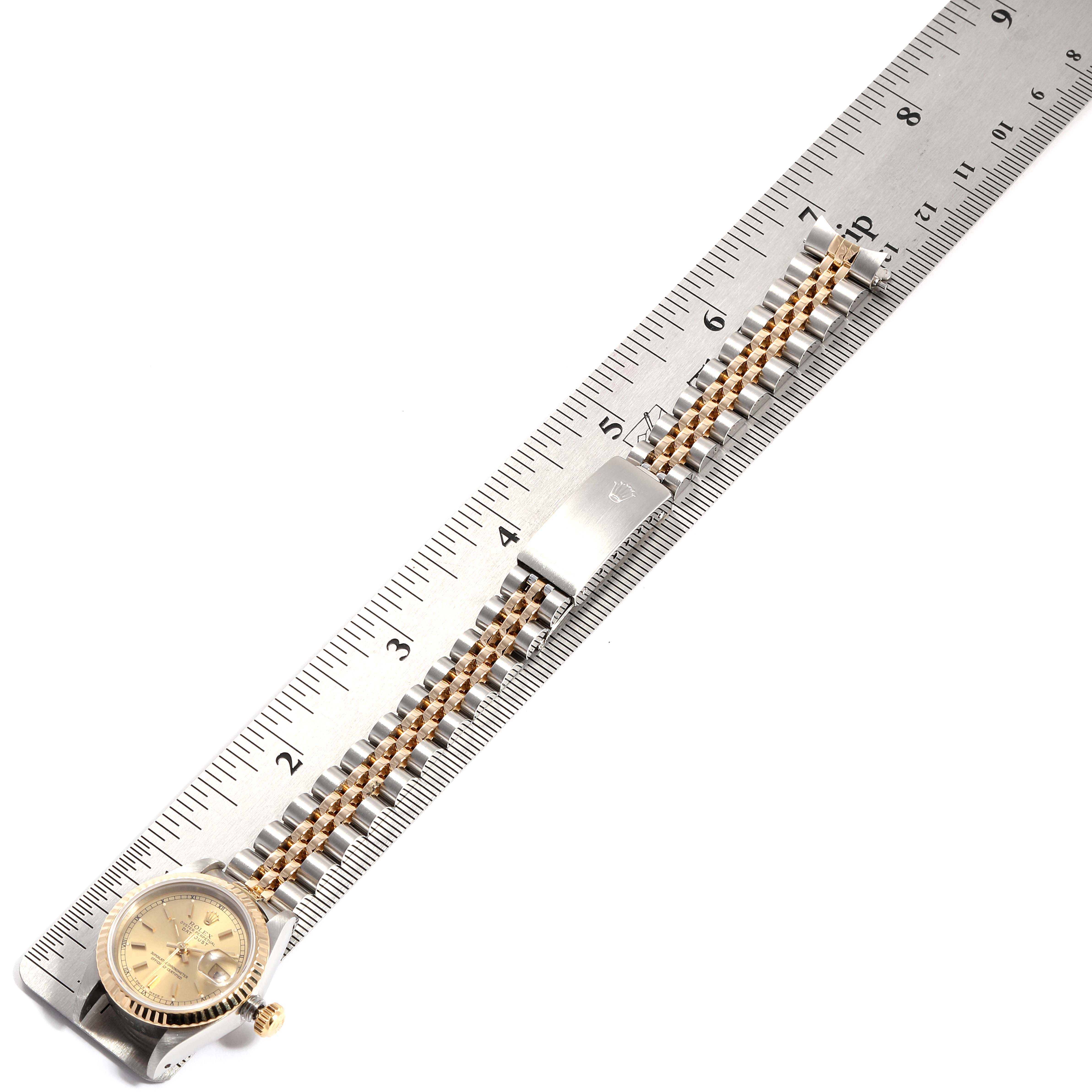 The Rolex Datejust 69173 Women's Steel and Gold (two tone) Champagne Dial 69173 Women's Steel and Gold (two tone) Champagne Dial watch shown is laid flat beside a ruler, displaying its face, bracelet, and clasp.