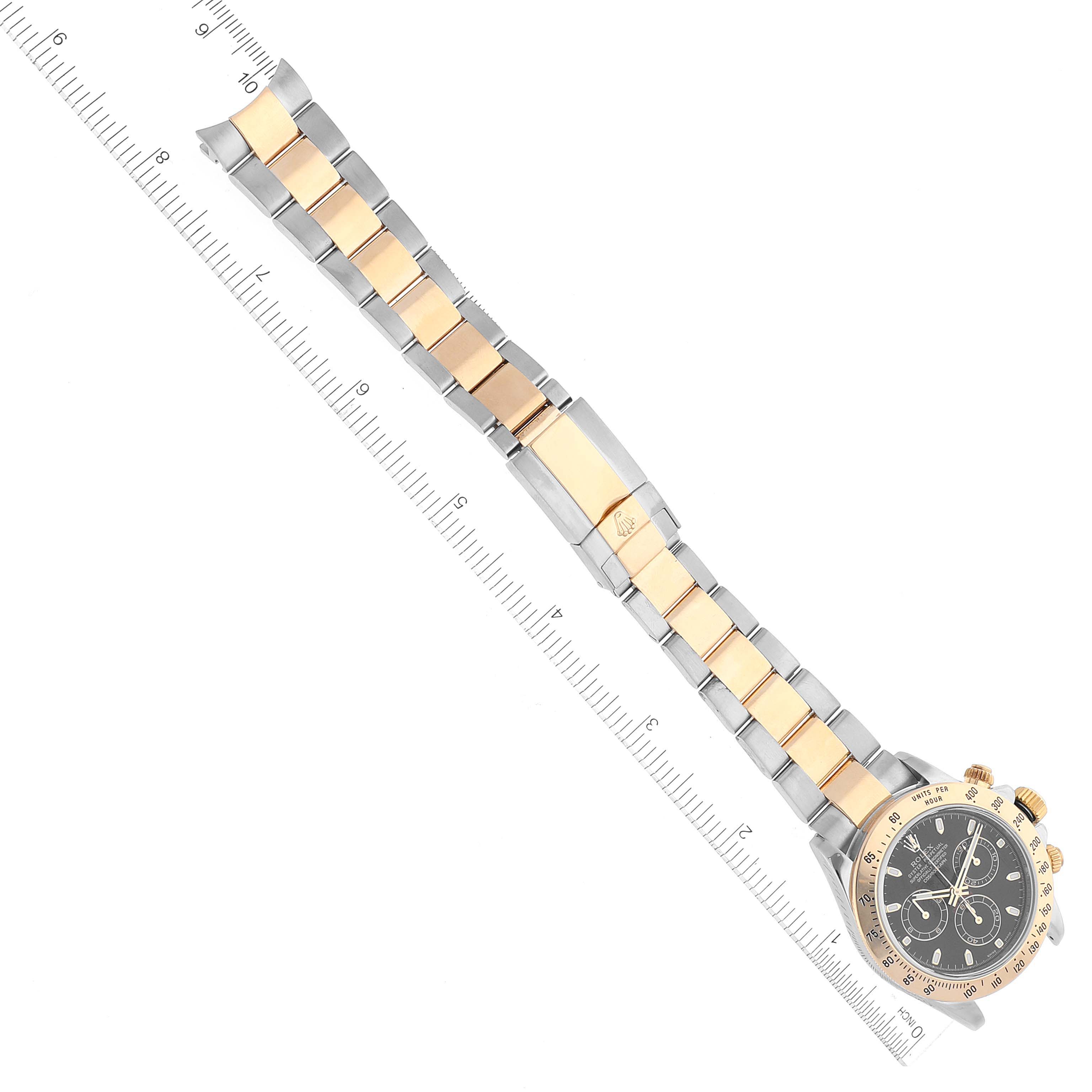 The image shows a Rolex Daytona 116523 Men's Steel and Gold (two tone) Black Dial 116523 Men's Steel and Gold (two tone) Black Dial watch at an angled top view with a full view of the bracelet aligned with a ruler.