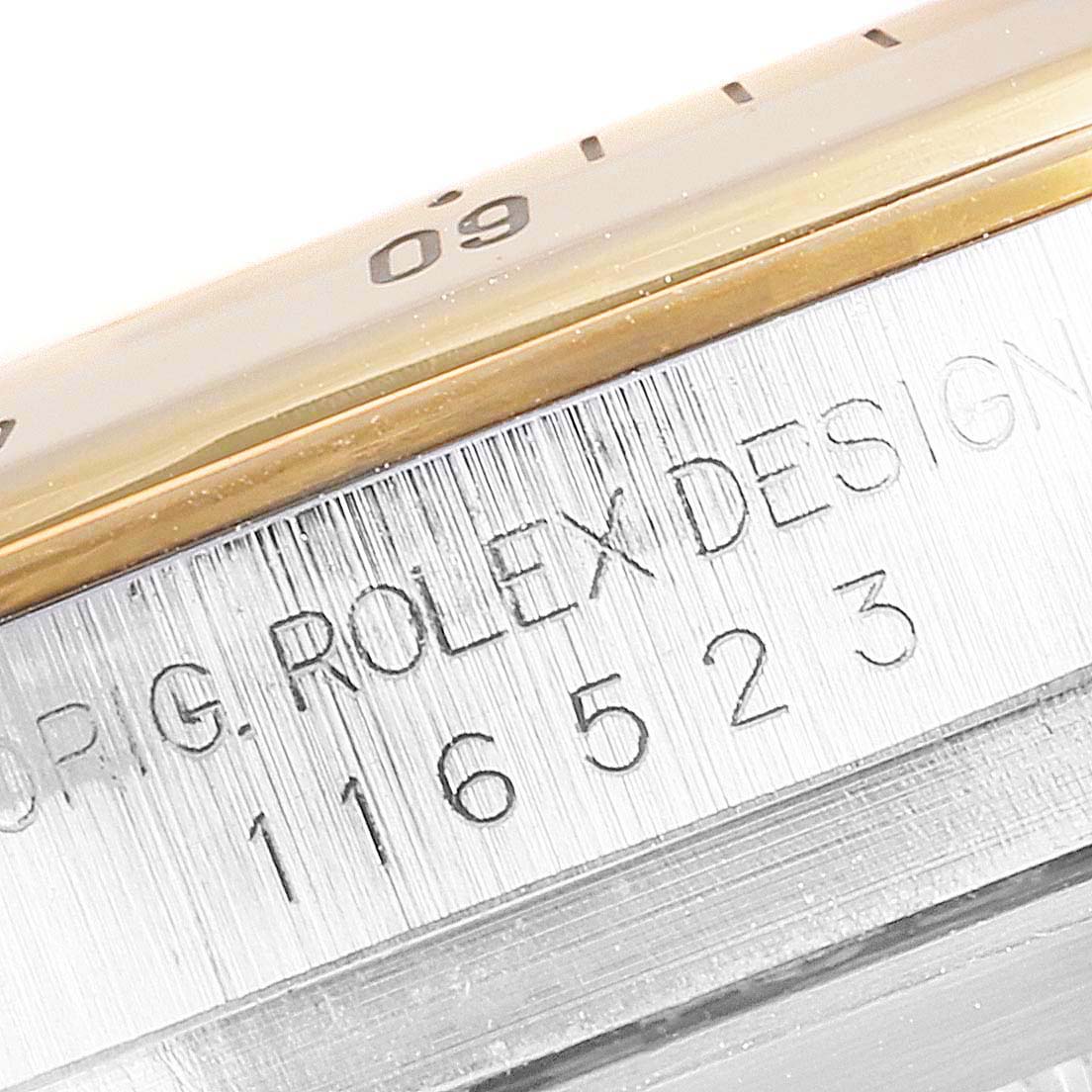 This close-up of a Rolex Daytona 116523 Men's Steel and Gold (two tone) White Dial 116523 Men's Steel and Gold (two tone) White Dial watch shows part of the bezel and the engraved edge with a model number.