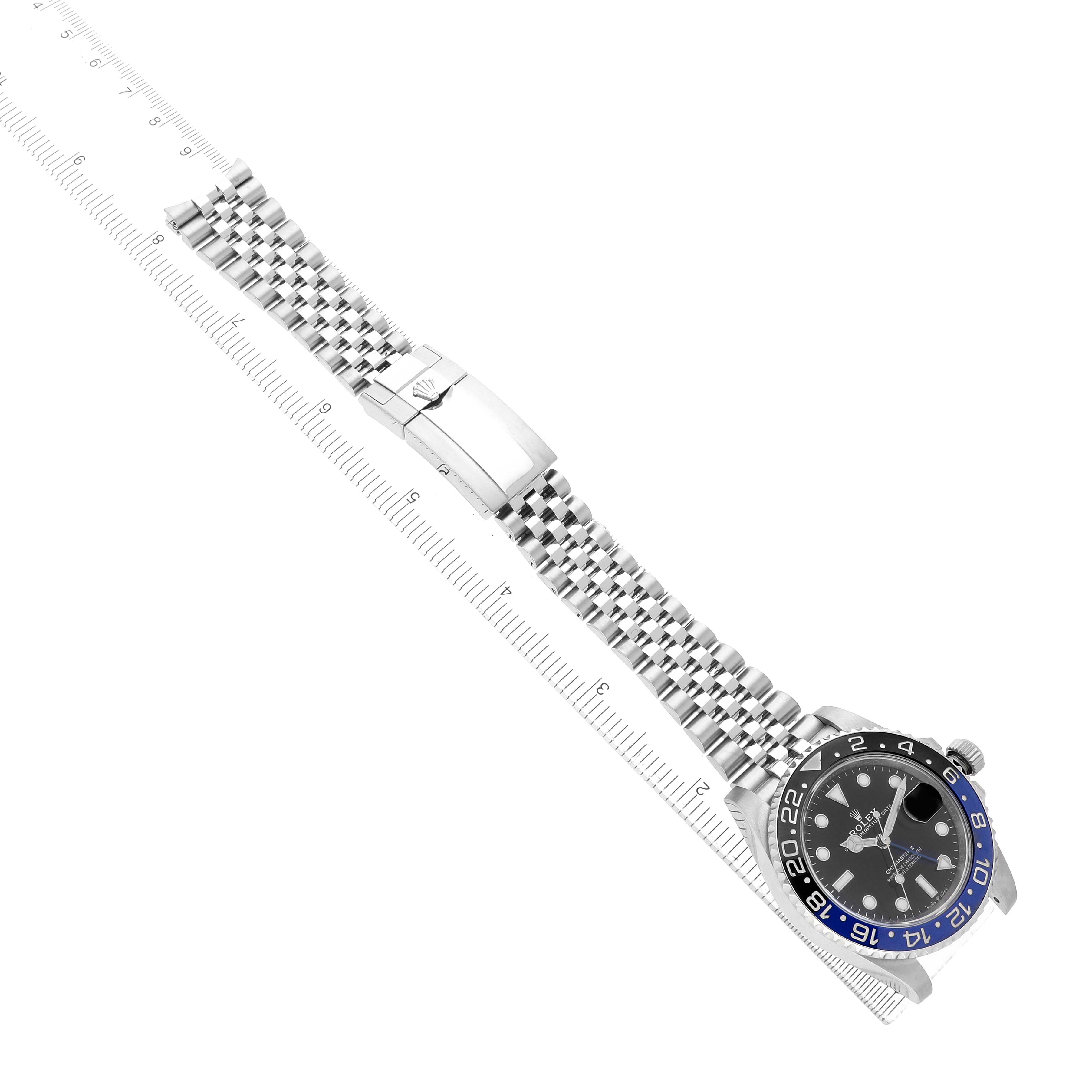 The Rolex GMT-Master 126710 Men's Stainless Steel Black Dial watch is shown at an angle highlighting the face, bezel, bracelet, and clasp, set against a measuring guide.