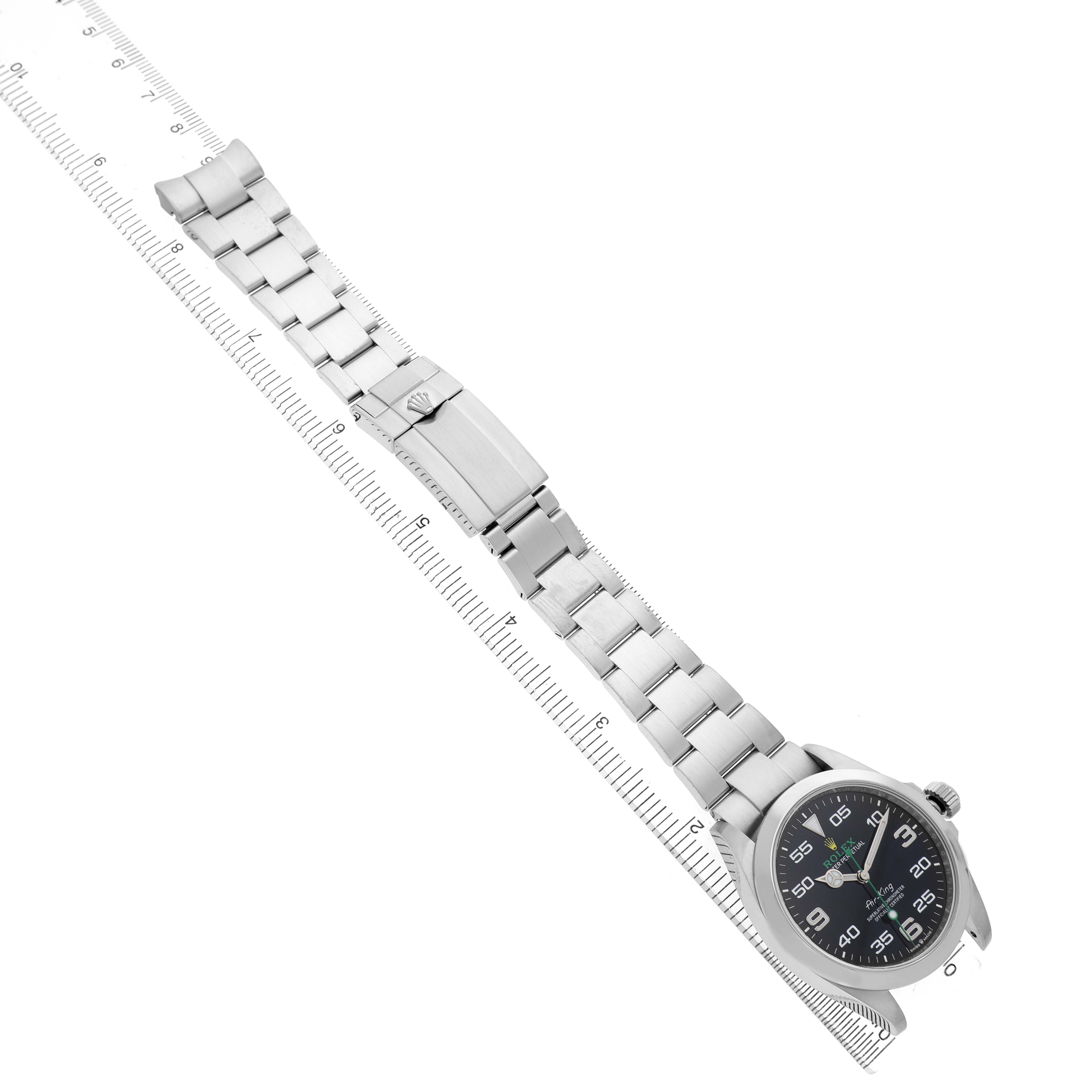 The Rolex Air-King 126900 Men's Stainless Steel Black Dial watch is shown at a diagonal angle, displaying the face, bezel, and full bracelet alongside a ruler.