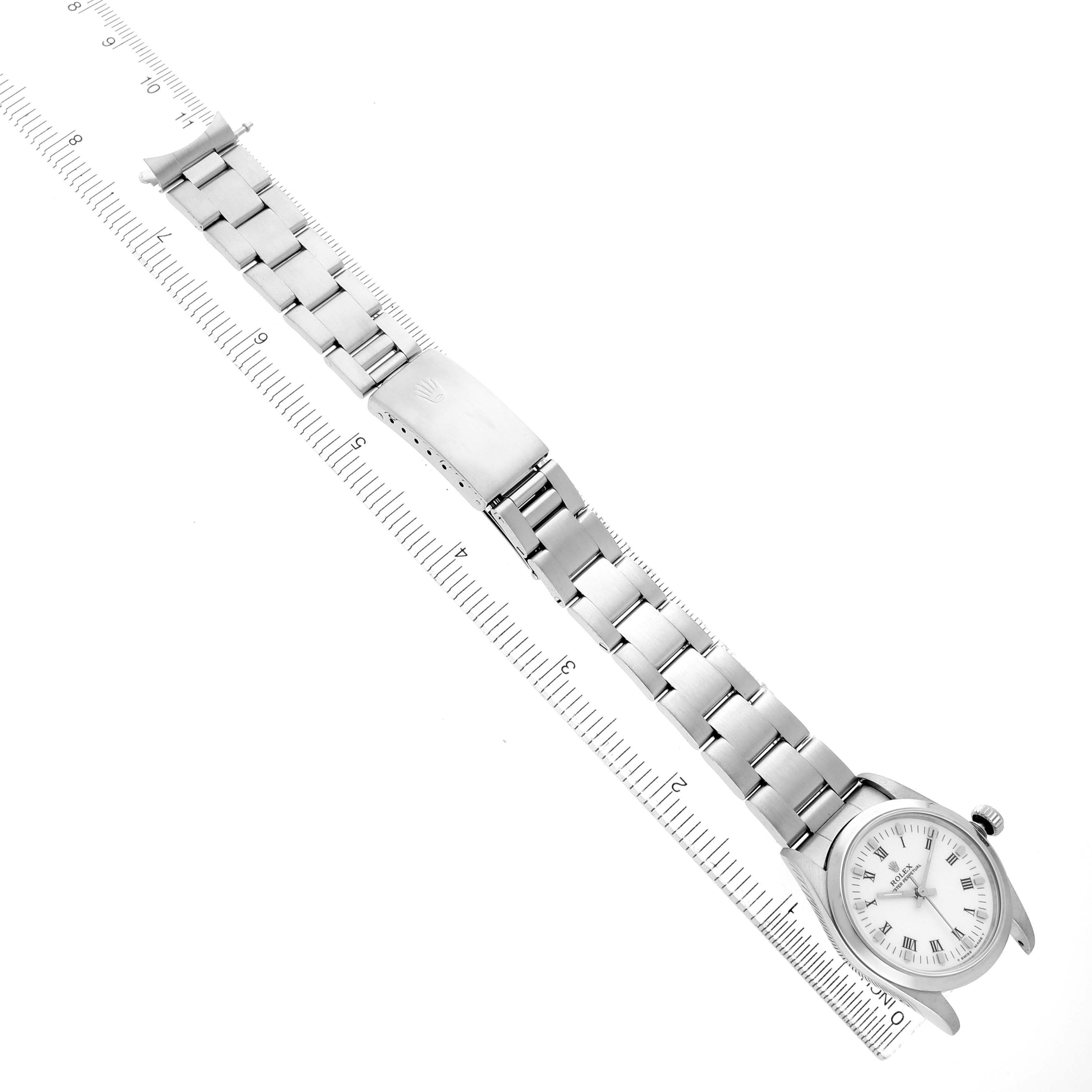 The Rolex Oyster Perpetual 67480 Women's Stainless Steel White Dial watch is shown from a top angle, displaying its full bracelet, clasp, and face alongside a ruler.