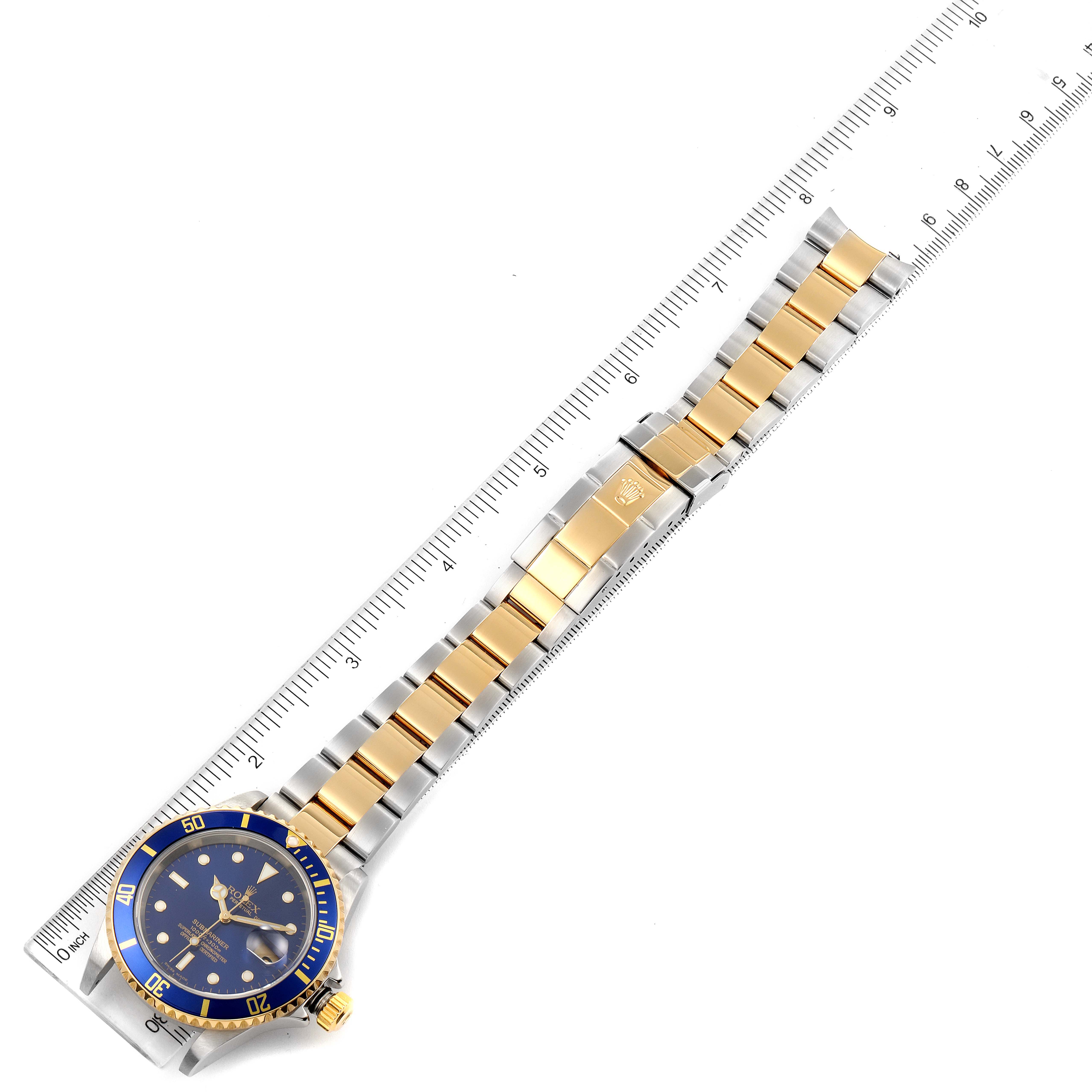 The image shows a Rolex Submariner 16613 Men
s Steel and Gold (two tone) Blue Dial 16613 Men
s Steel and Gold (two tone) Blue Dial watch laid flat next to a ruler, capturing the full length of the band and face.