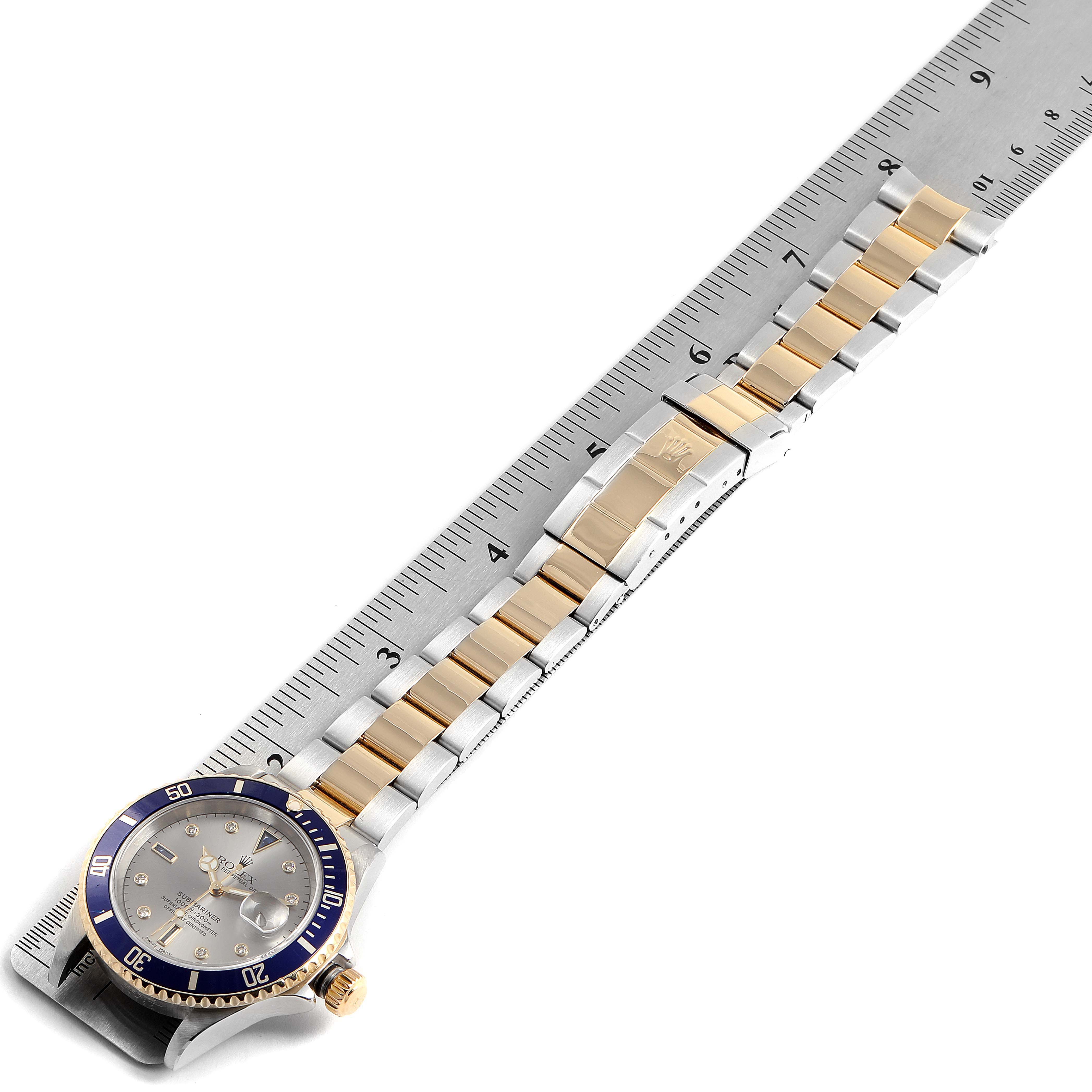 The image shows a Rolex Submariner 16613 Men's Steel and Gold (two tone) Grey Dial 16613 Men's Steel and Gold (two tone) Grey Dial watch lying flat on a ruler, displaying the face and bracelet at an angle.