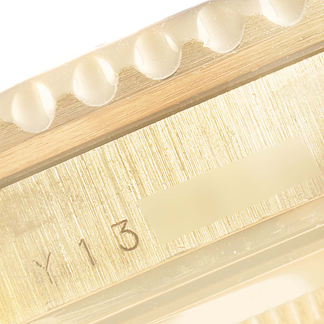 This close-up image shows the edge of the Rolex Submariner 16618 Men's Yellow Gold Blue Dial 16618 Men's Yellow Gold Blue Dial's bezel and part of its engraved serial number on the case.