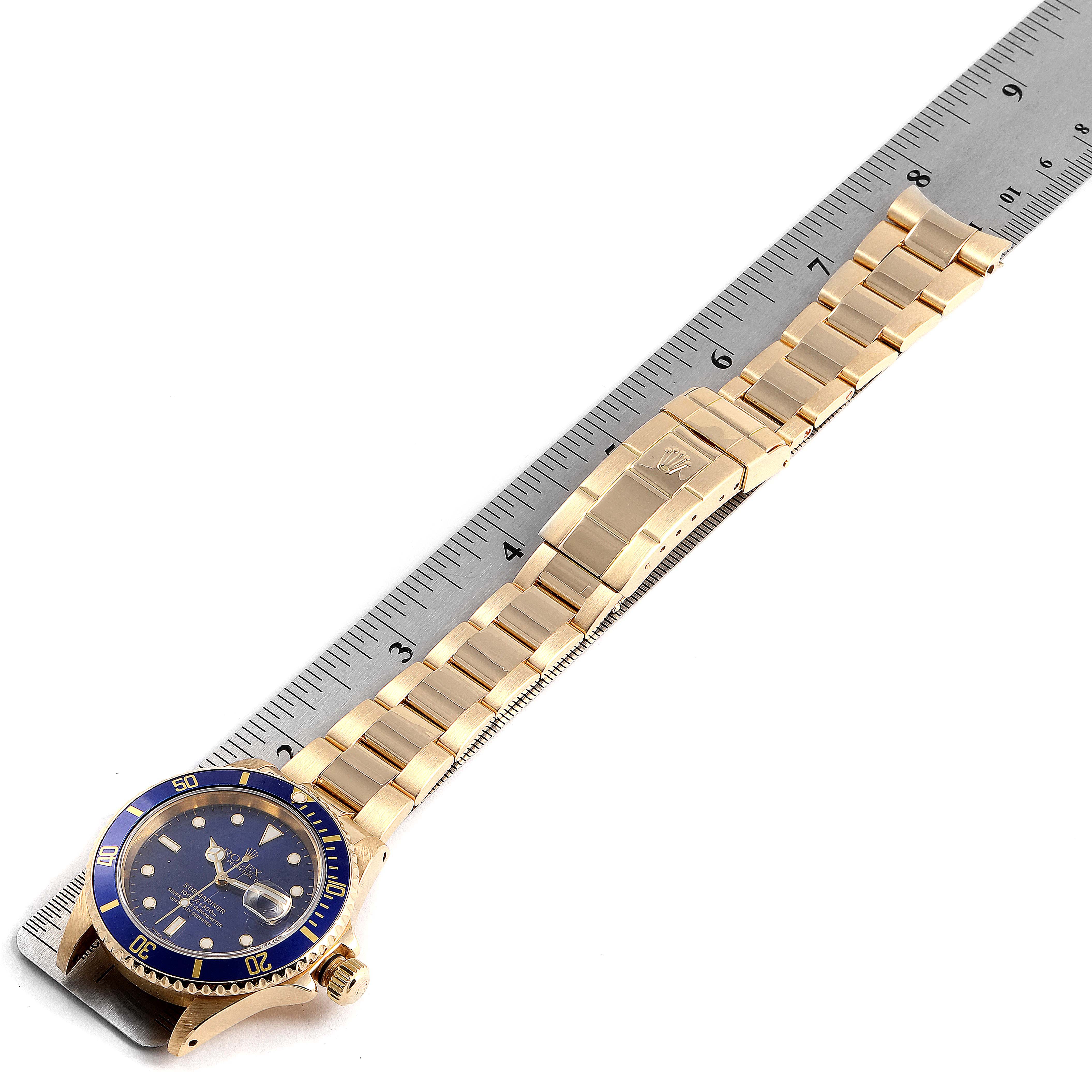 The Rolex Submariner 16618 Men's Yellow Gold Blue Dial 16618 Men's Yellow Gold Blue Dial watch is shown in a top-down view, displaying the face, bezel, bracelet, and clasp alongside a ruler for measurement.