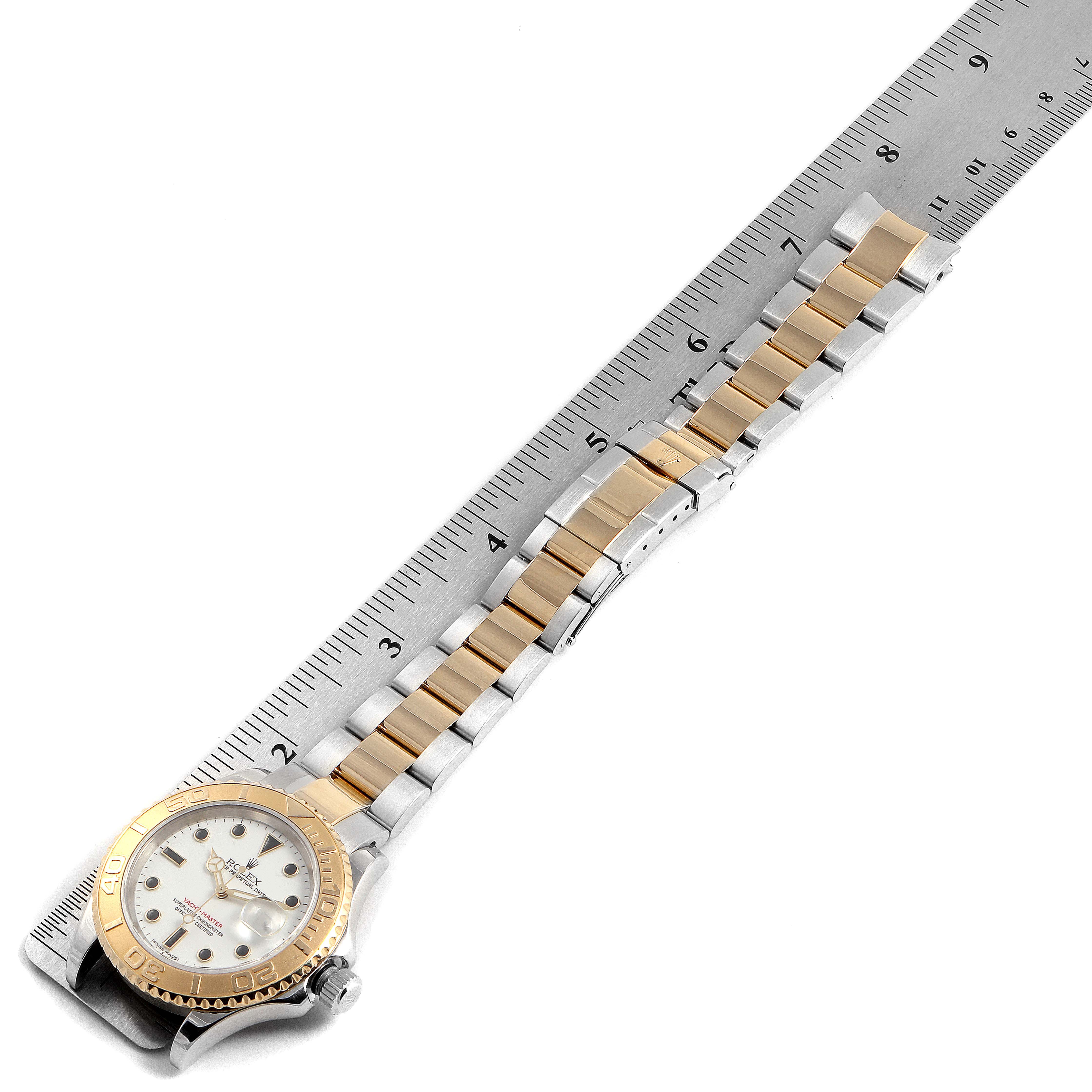 This image shows the Rolex Yacht-Master 16623 Men's Steel and Gold (two tone) White Dial 16623 Men's Steel and Gold (two tone) White Dial watch laying flat with a ruler, displaying its gold bezel, dial, and two-tone metal bracelet.