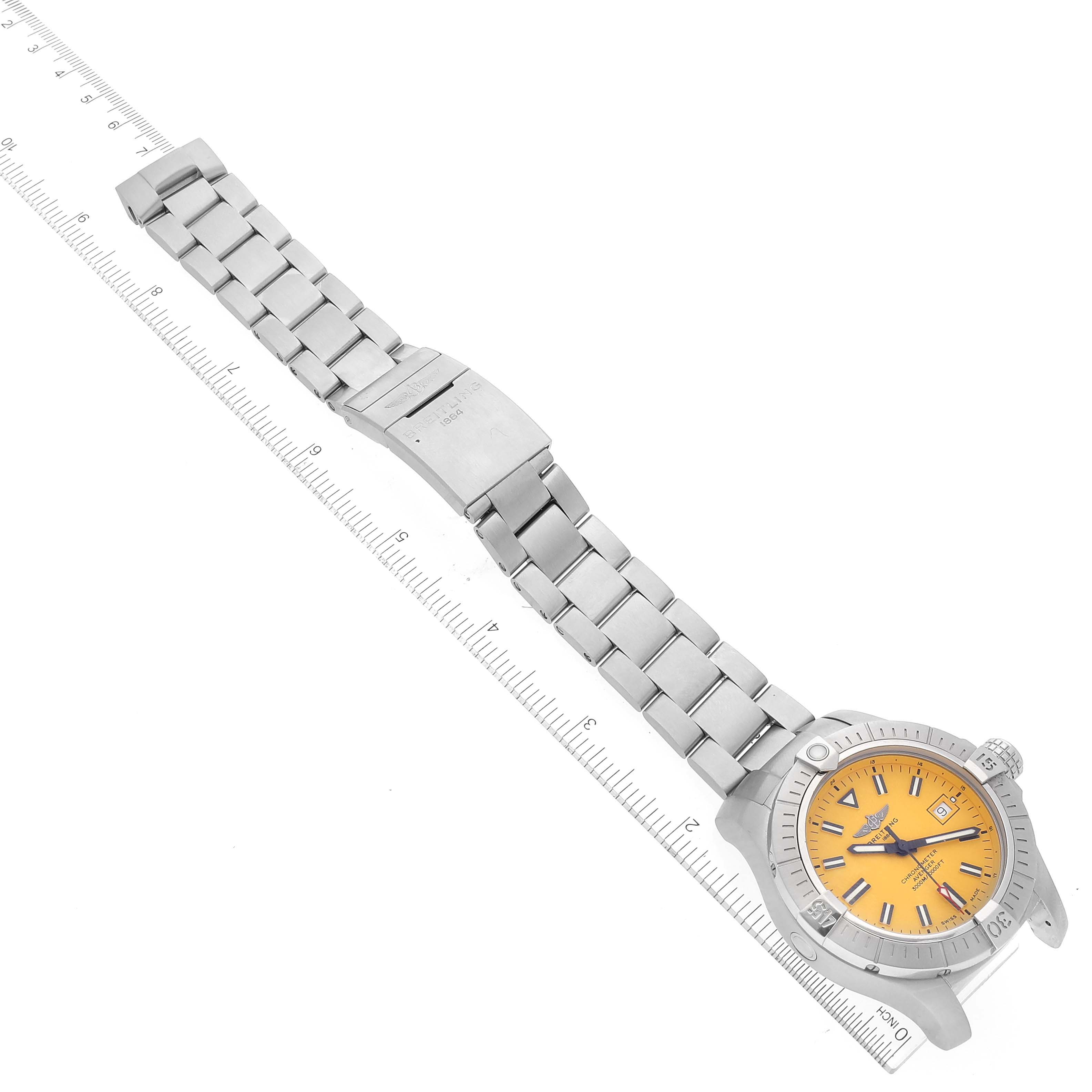 The image shows a top-down view of a Breitling Avenger A17319 Men's Stainless Steel Yellow Dial A17319 Men's Stainless Steel Yellow Dial watch with a yellow dial and a metal bracelet, along with a ruler for scale.