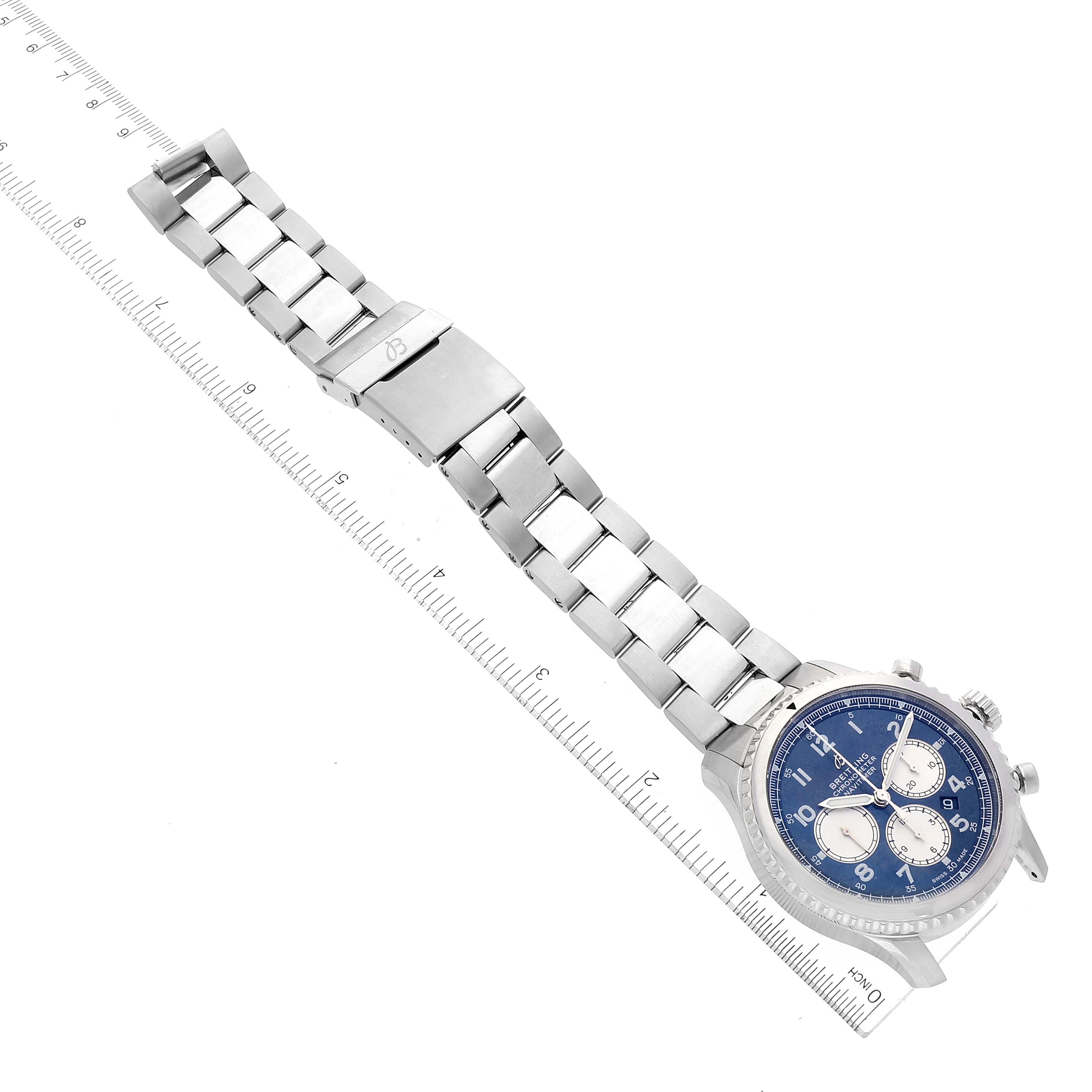 The image shows a Breitling Navitimer watch lying flat, with its metal bracelet and clasp fully extended alongside a ruler for scale.