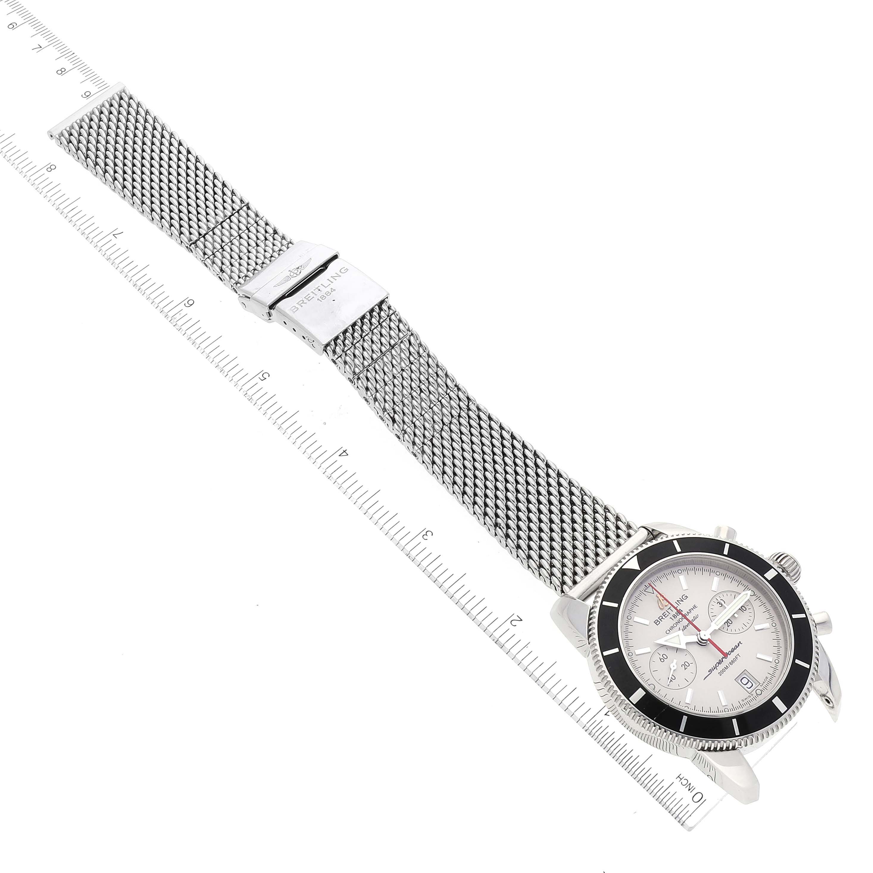 The image shows a top-down view of a Breitling Superocean A23370 Men
s Stainless Steel Silver Dial A23370 Men
s Stainless Steel Silver Dial watch with a mesh bracelet next to a ruler for scale.