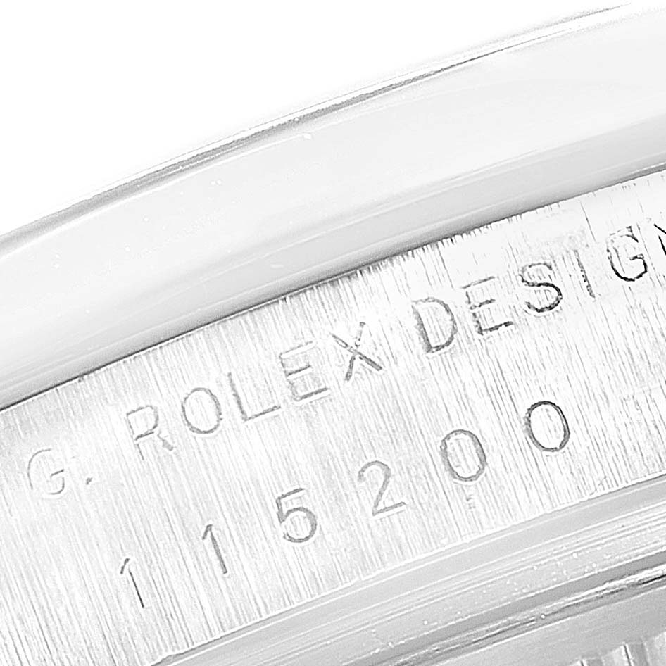 The image shows an extreme close-up of the case back, featuring the serial number and "Rolex Design" text on a Rolex Date 115200 Men's Stainless Steel Black Dial 115200 Men's Stainless Steel Black Dial model.