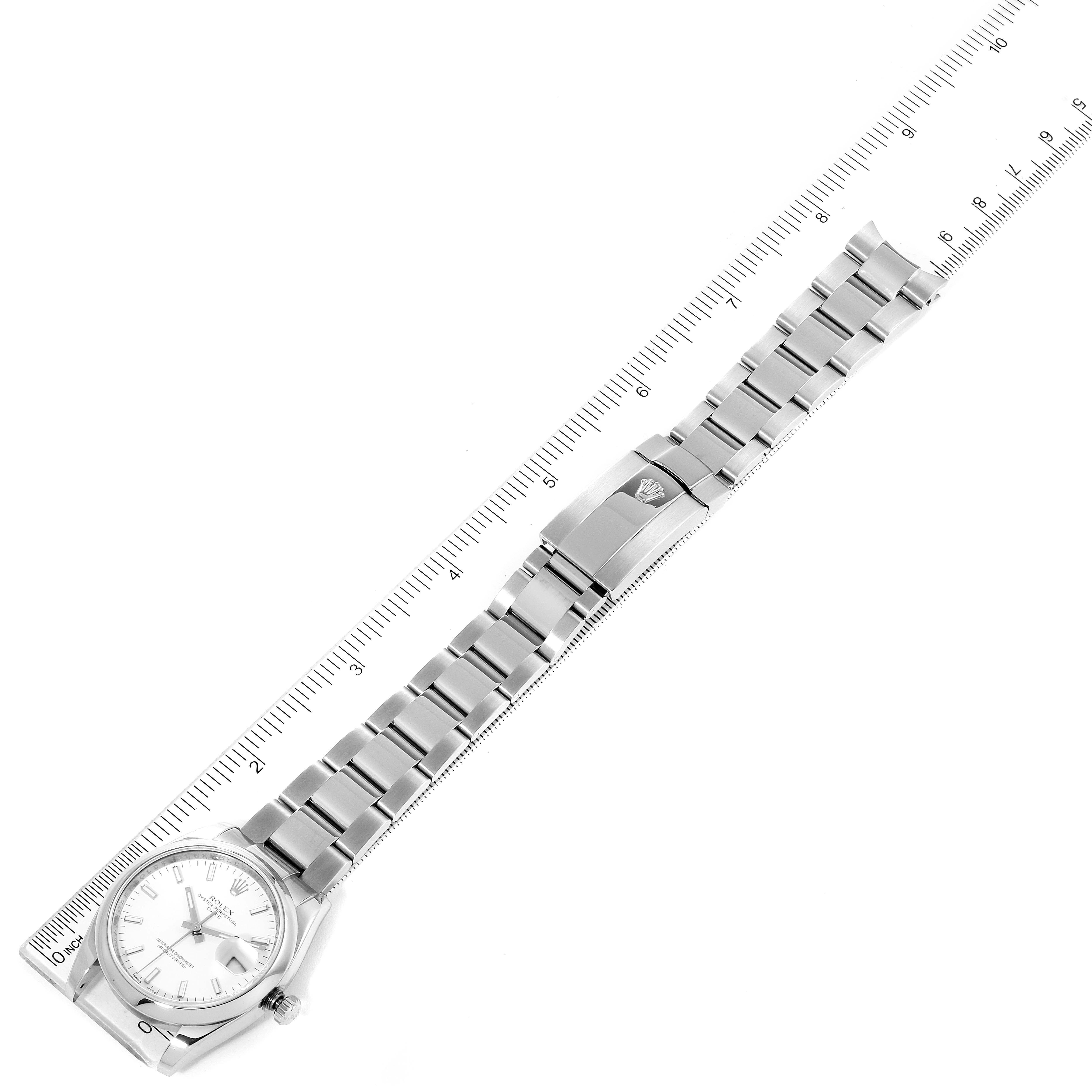 The Rolex Date 115200 Men's Stainless Steel White Dial 115200 Men's Stainless Steel White Dial model watch is shown laying flat with its dial, bracelet, and clasp in view, along with a ruler for scale.