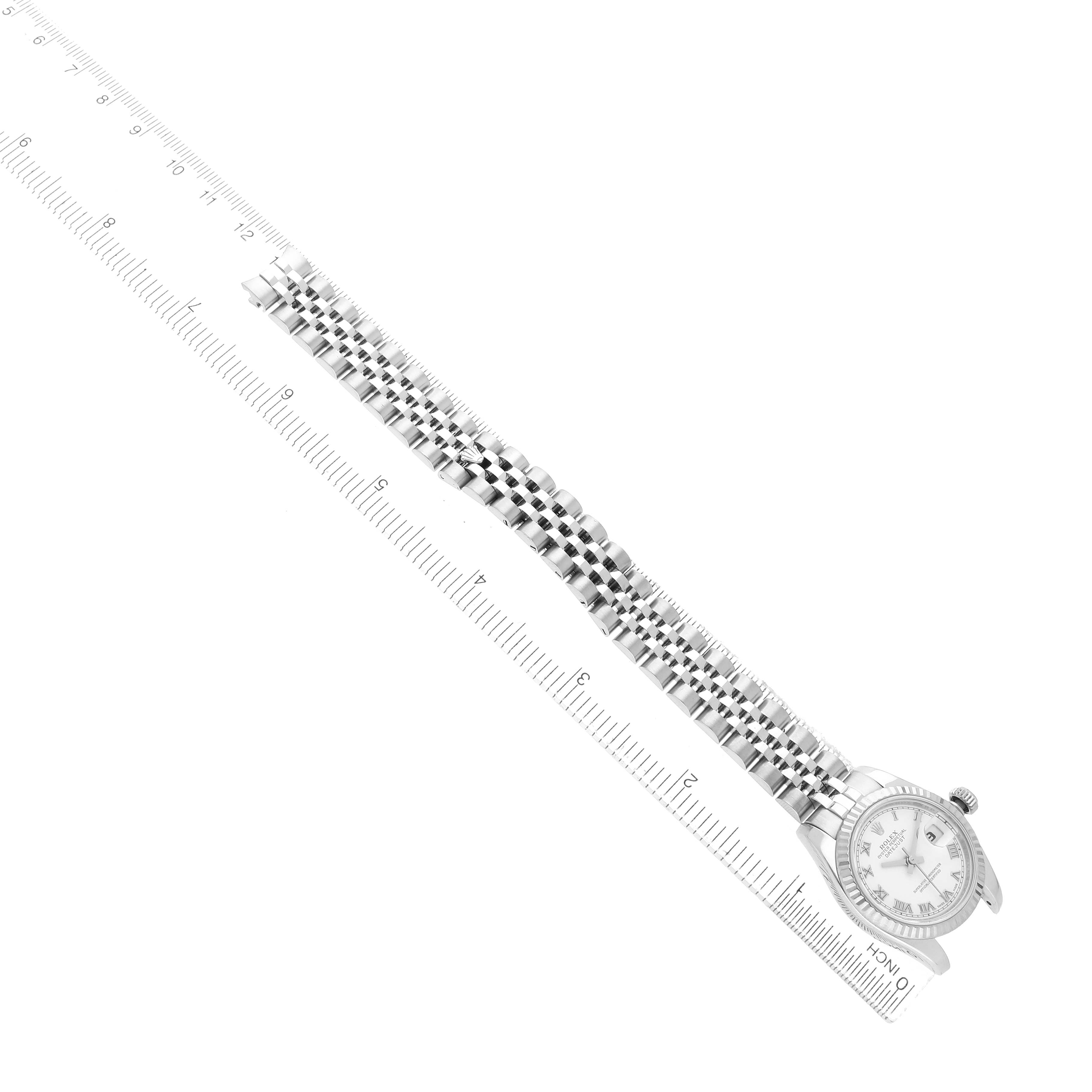 The Rolex Datejust 179174 Women's Stainless Steel White Dial watch is shown from a top-down view, displaying the face, bracelet, and a measuring ruler.