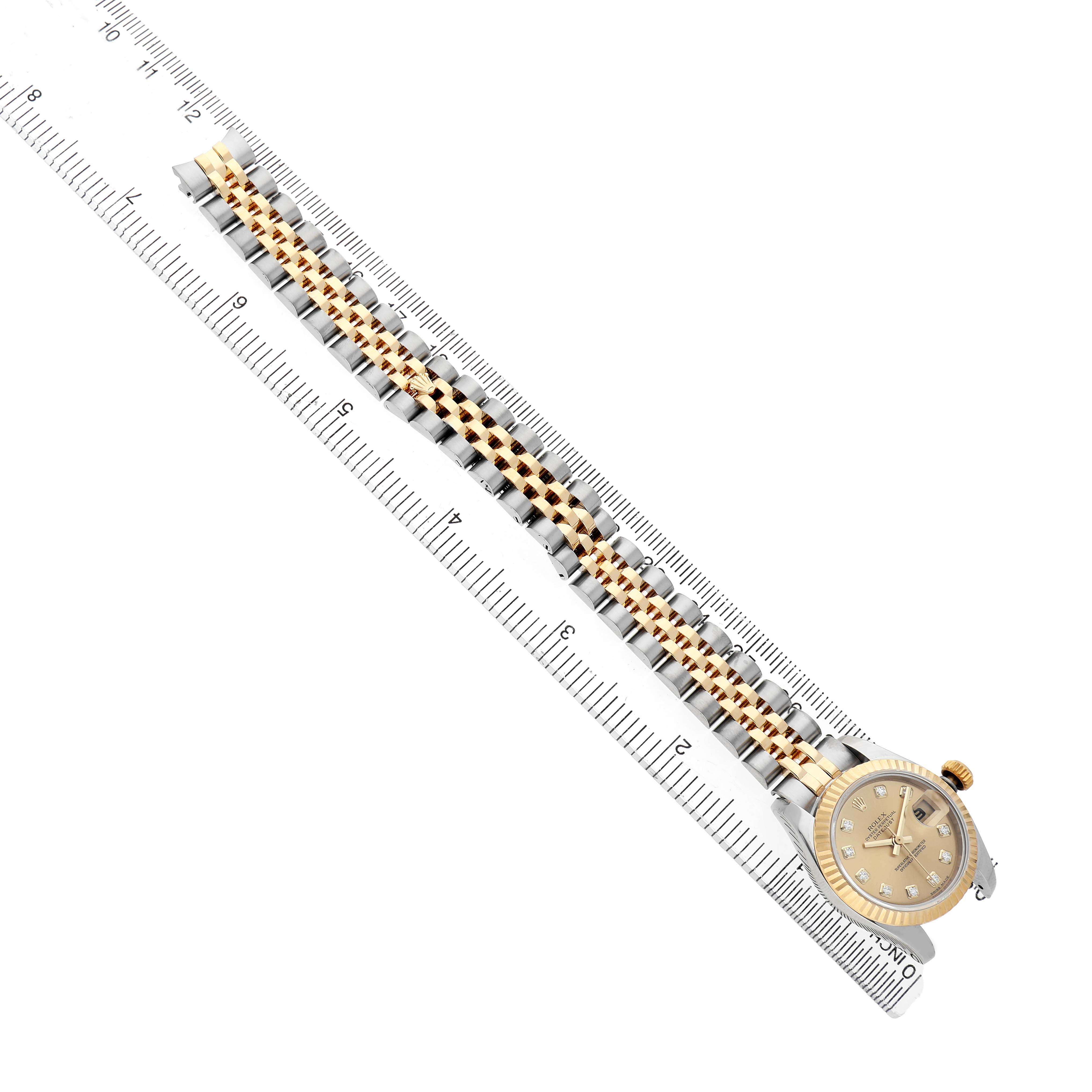 The Rolex Datejust 179173 Women's Steel and Gold (two tone) Champagne Dial watch is shown from an aerial view, displaying the full bracelet and dial alongside a ruler.